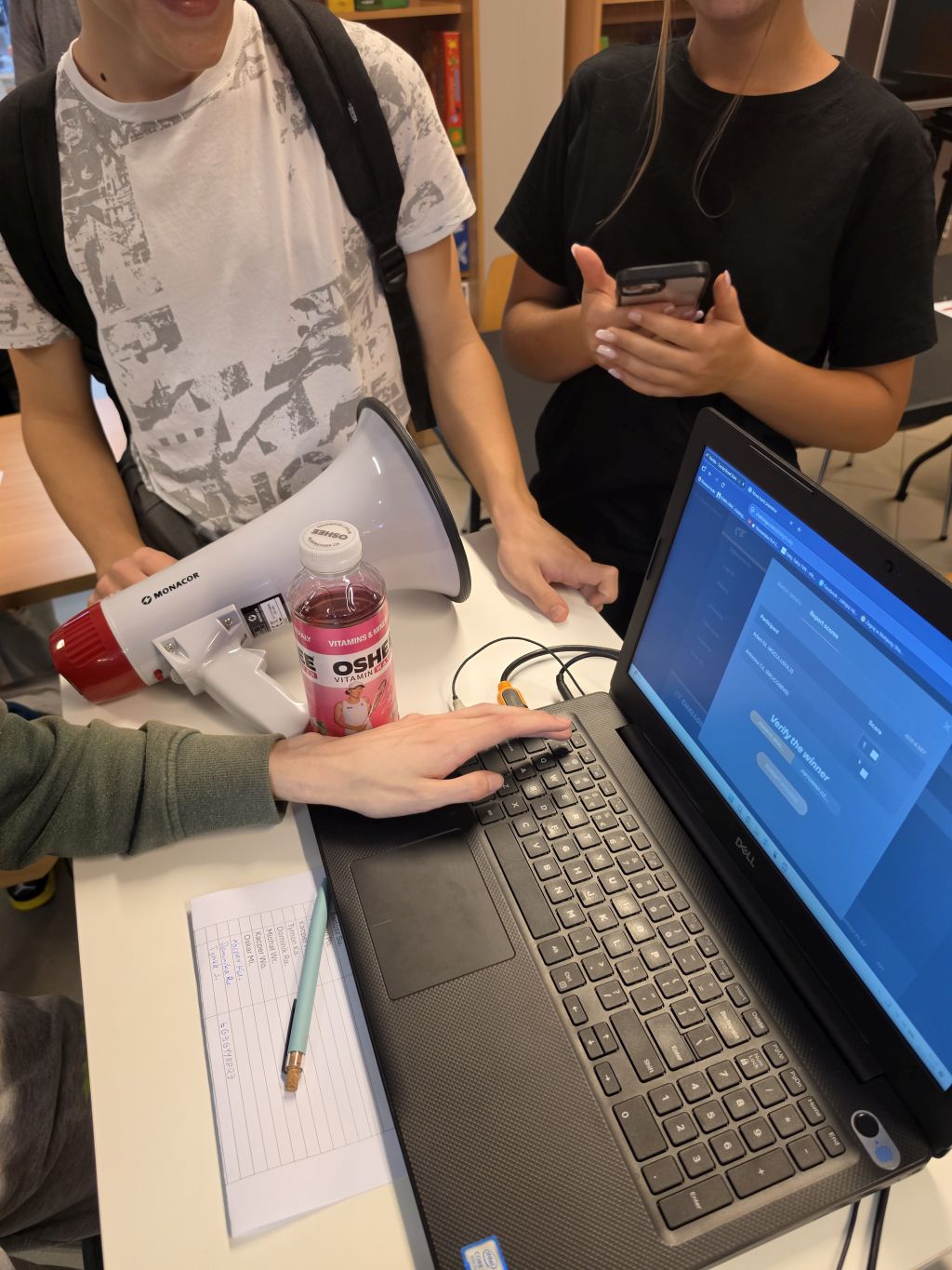 Laptop, megafon i dwie osoby stojące przy stanowisku.