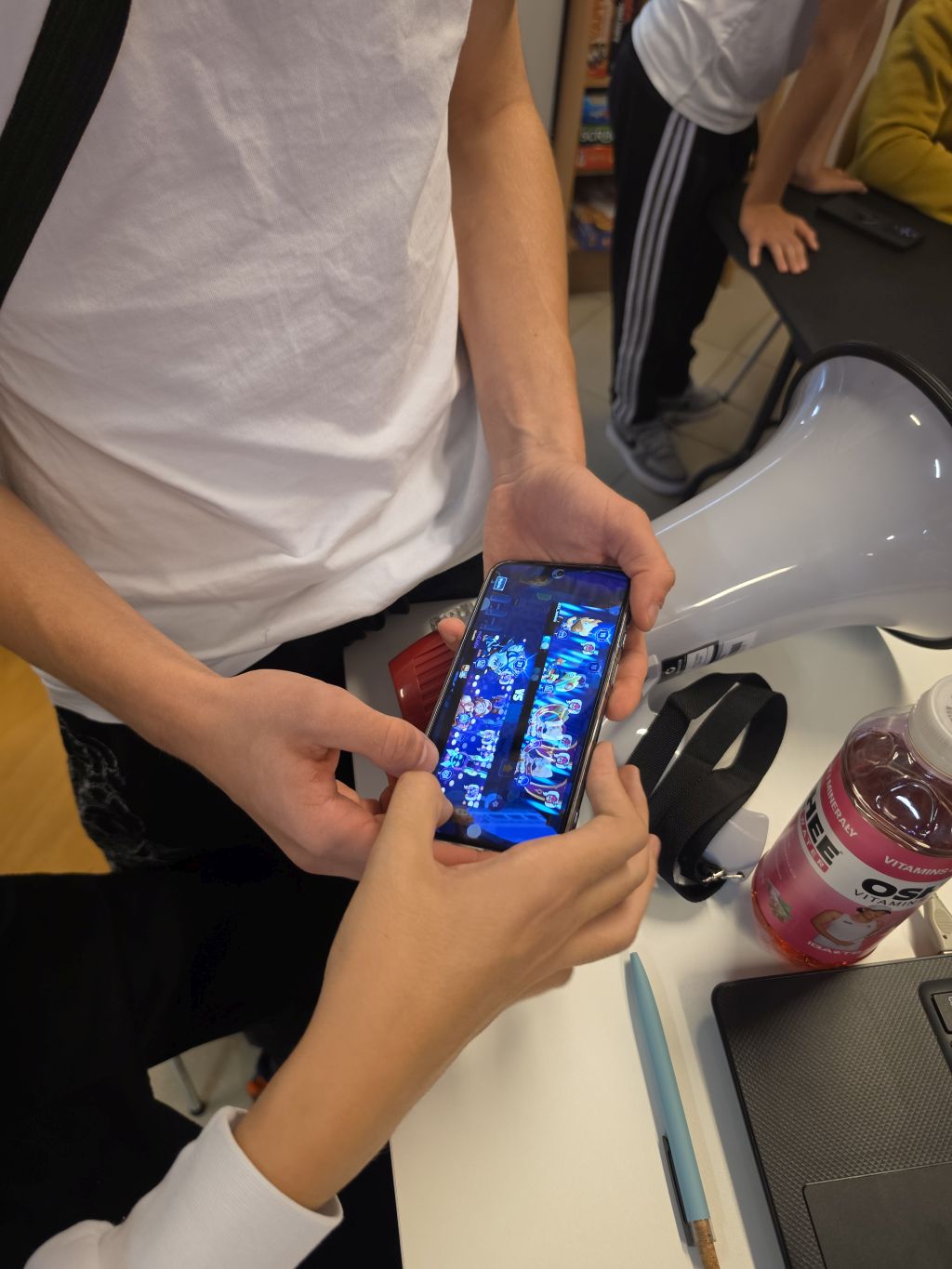 Dwie osoby oglądają ekran smartfona obok megafonu i laptopa.