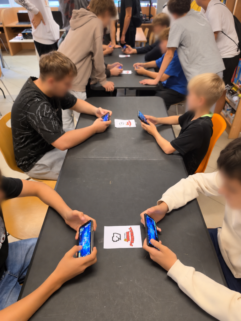 Kilka osób gra na smartfonach przy długim czarnym stole.