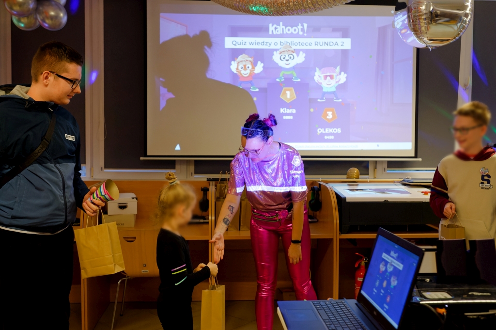 Kobieta w różowym stroju wręcza nagrodę dziewczynce podczas quizu Kahoot.