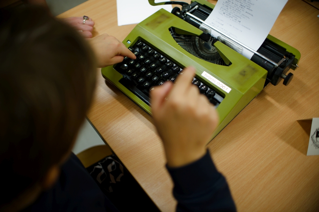 Dziecko pisze na zielonej maszynie do pisania w strefie biblioteki retro.