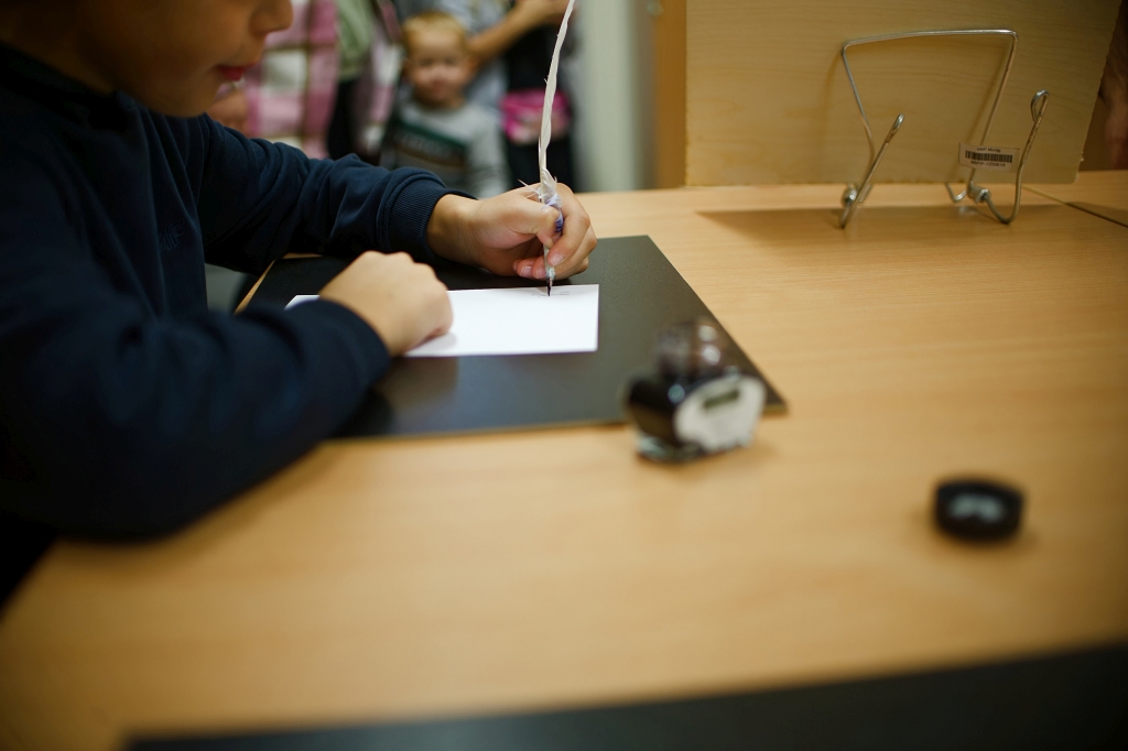 Dziecko pisze gęsim piórem na kartce papieru podczas pokazu dawnych technik pisania.