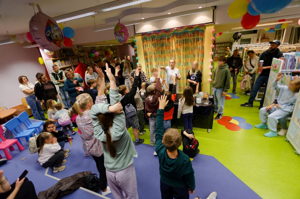 Grupa dzieci podnosi ręce podczas zabawy prowadzonej w Dziale dla Dzieci.