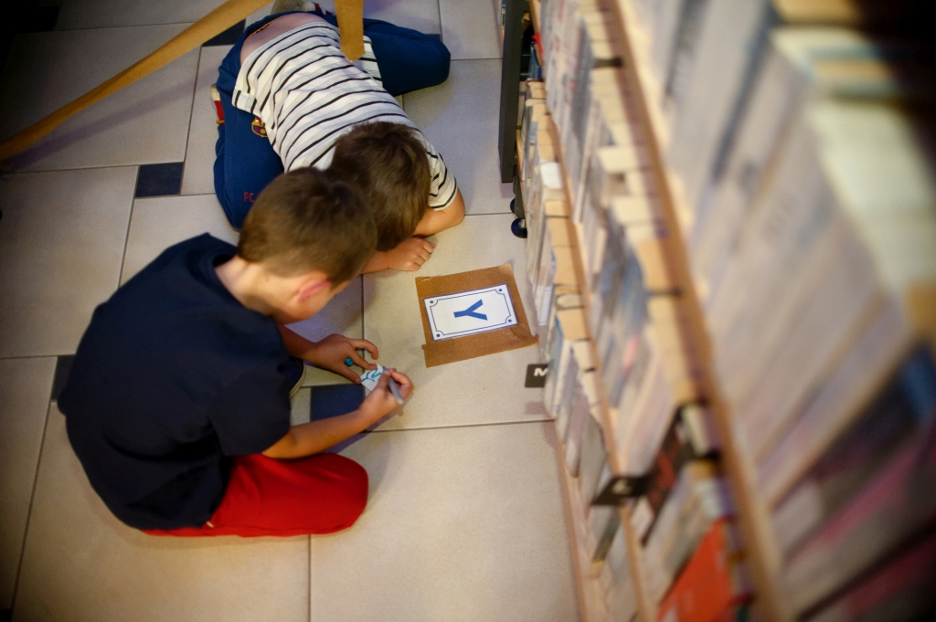 Dwóch chłopców rozwiązuje zadanie przy regale z książkami podczas gry bibliotecznej.