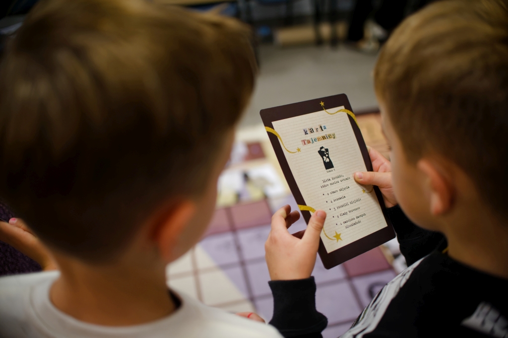Dwóch chłopców ogląda kartę tajemniczej misji podczas gry bibliotecznej.
