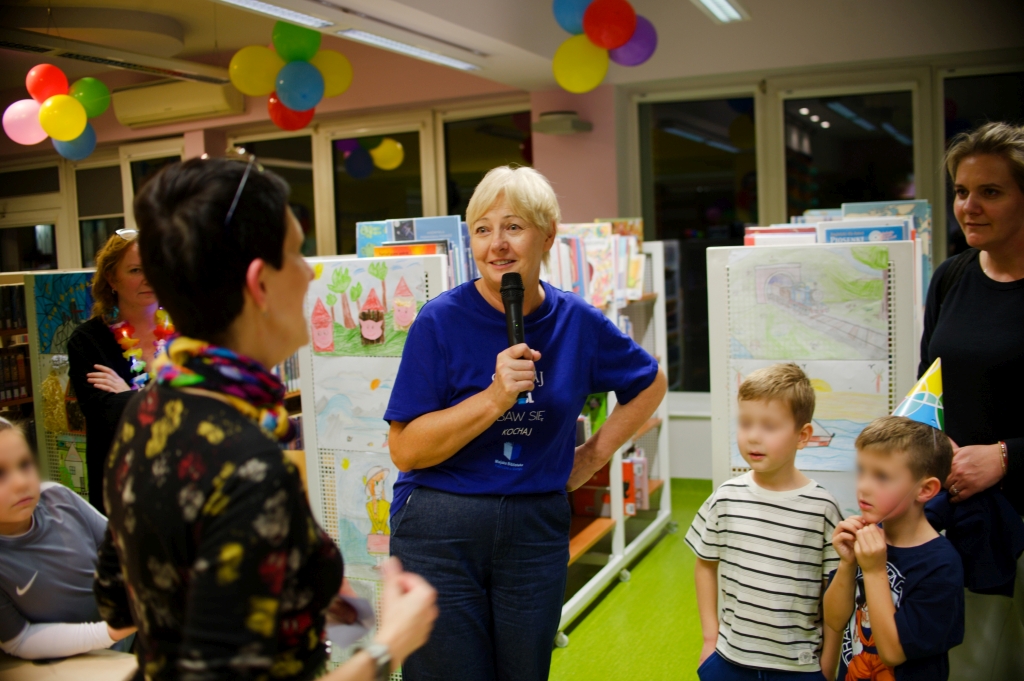 Bibliotekarka z mikrofonem rozmawia z uczestnikami jubileuszowej Nocy Bibliotek.
