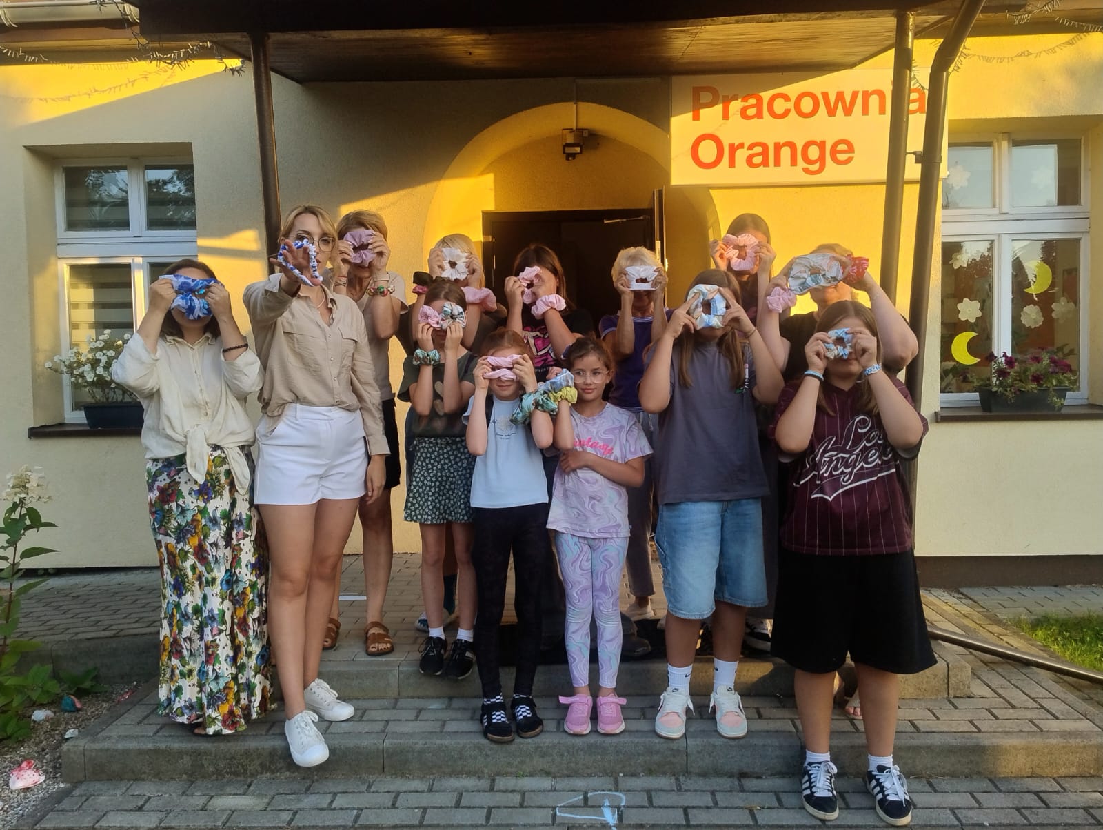 zdjęcie przedstawia grupę uczestników warsztatów, którzy trzymają własnoręcznie wykonaną scrunchie gumkę na twarzy