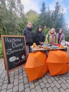 dwa parasole, tablica z napisem Pracownia Orange i cztery wolontariuszki