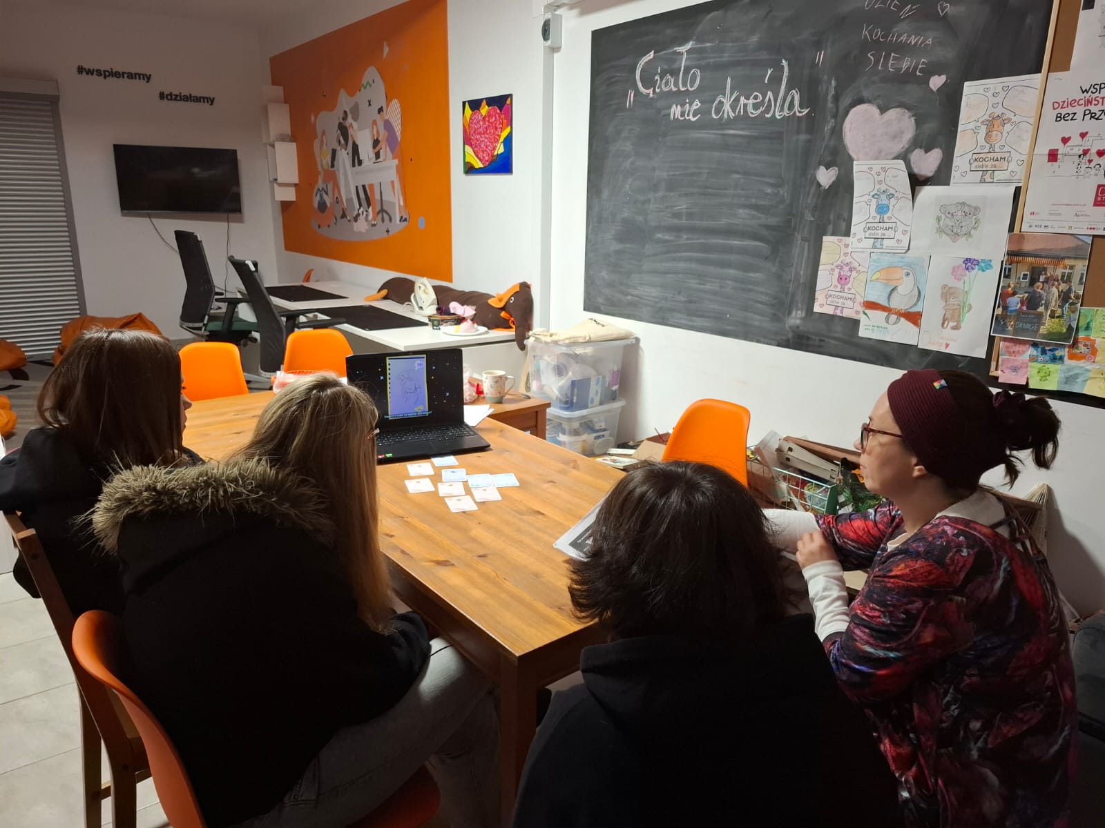 trzy osoby siedzą przy stole i oglądają spot Ciało nie określa