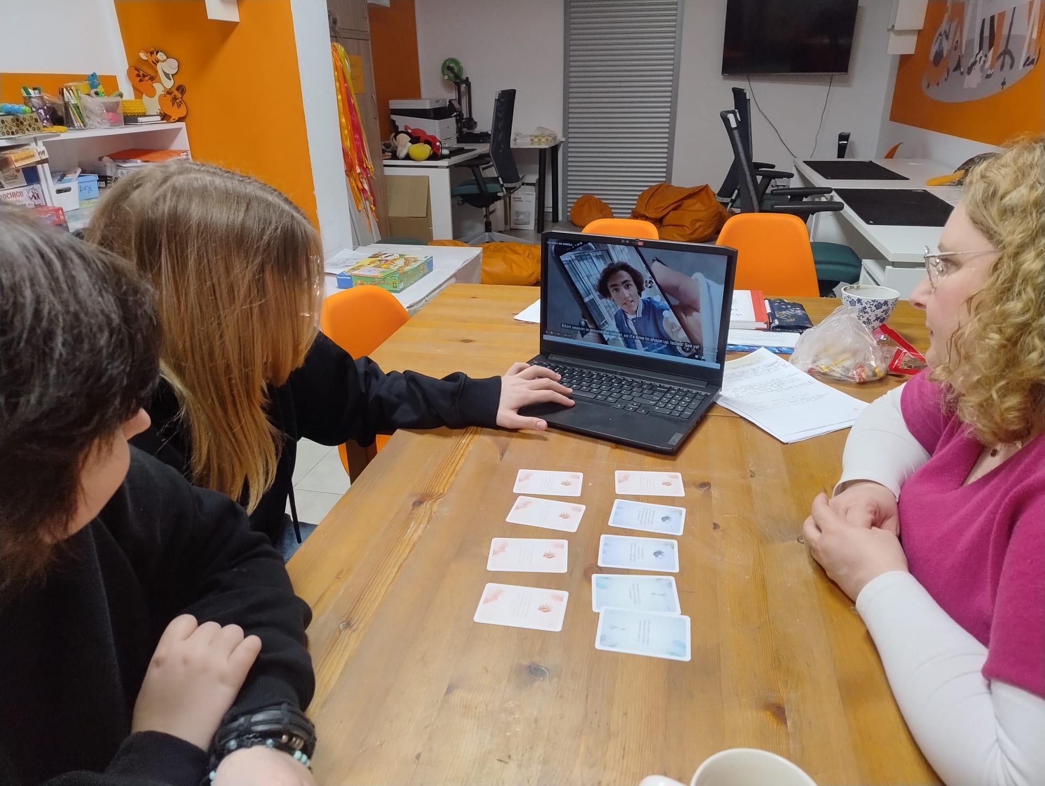 na zdjęciu trzy osoby oglądajace filmik Ciało nie określa, na stole leżą pomocnicze karty edukacyjne