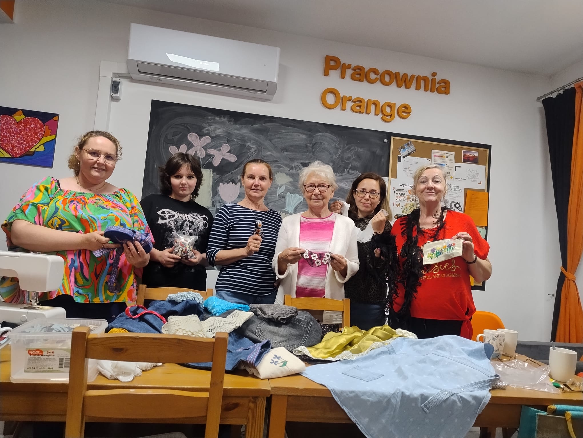 zdjęcie grupowe przedstawiające uczestniczki warsztatów, każda z nich trzyma w rkęu jakieś ubranie i dodatek pasmanteryjny