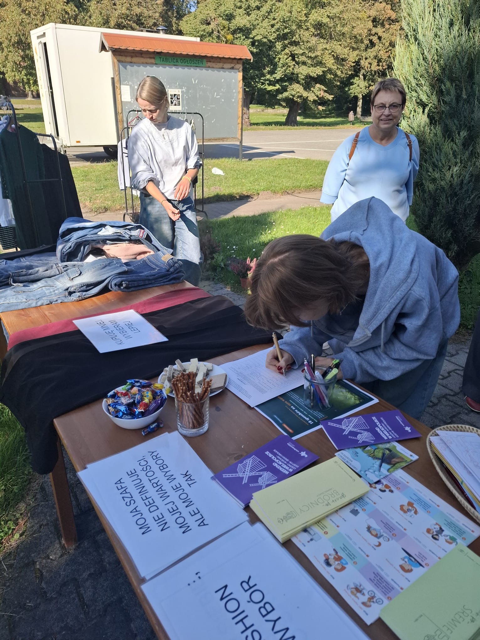Kilka osób zgromadzonych przy stołach z ubraniami.
