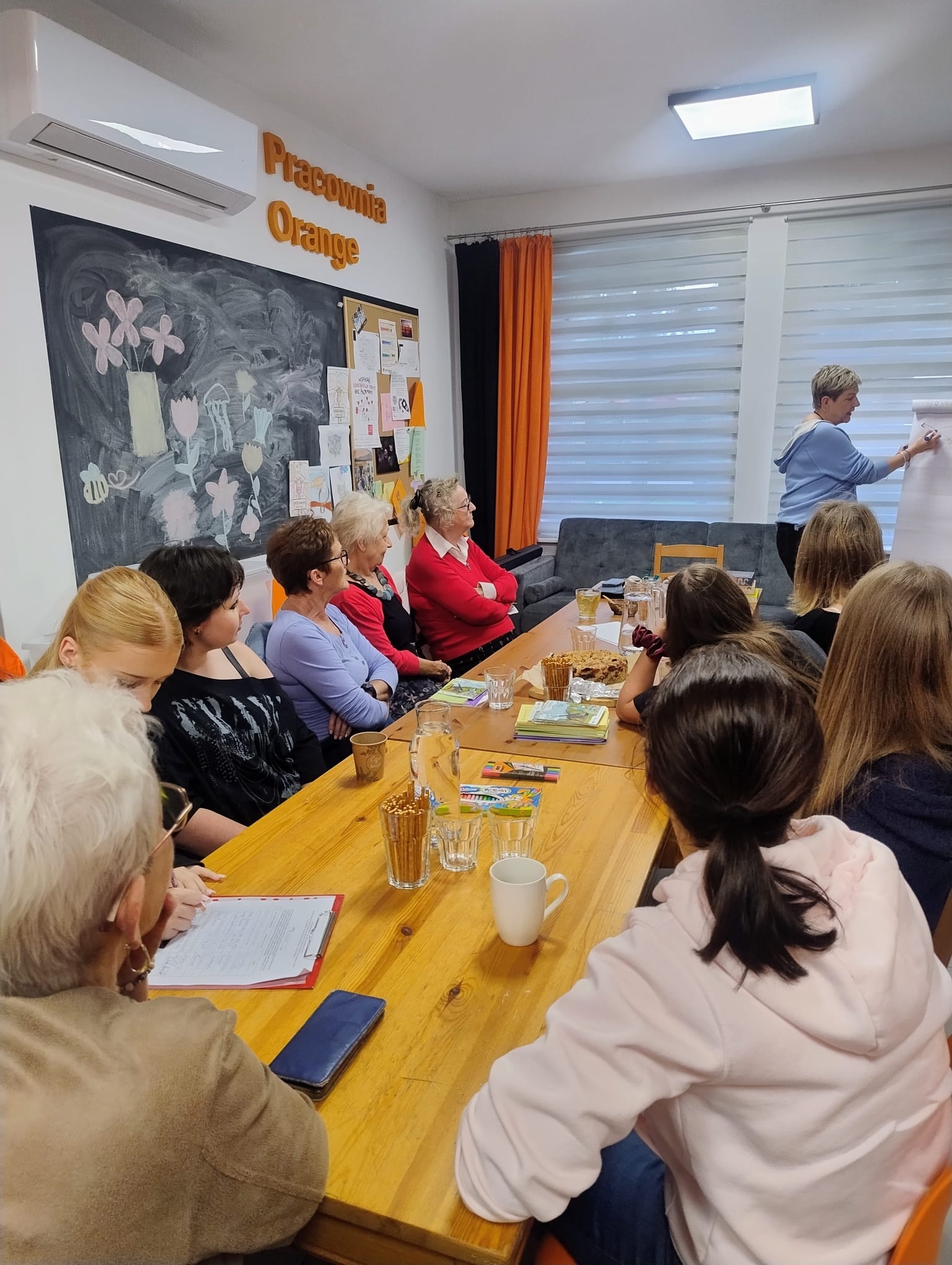 Grupa osób siedzących w Pracowni Orange podczas udziału w warsztatach.