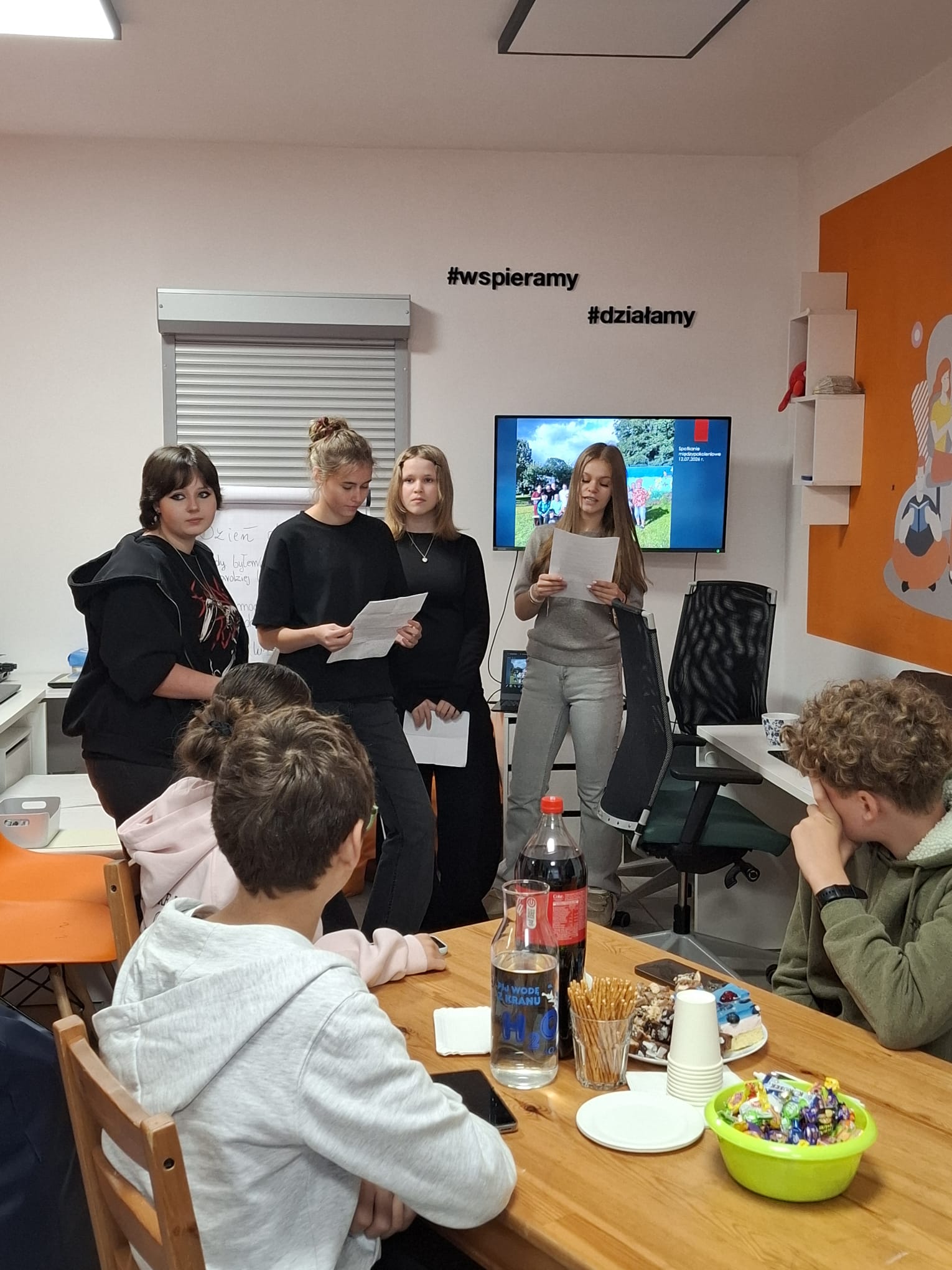 na zdjęciu widać młode osoby, które stoją i przedstawiają informacje o realizowanym projekcie