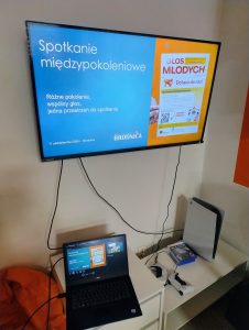 na zdjęciu ekran z wyświetloną prezentacją dotyczącą projektu: Głos Młodych. Laptop znajduje się na białym stoliku.