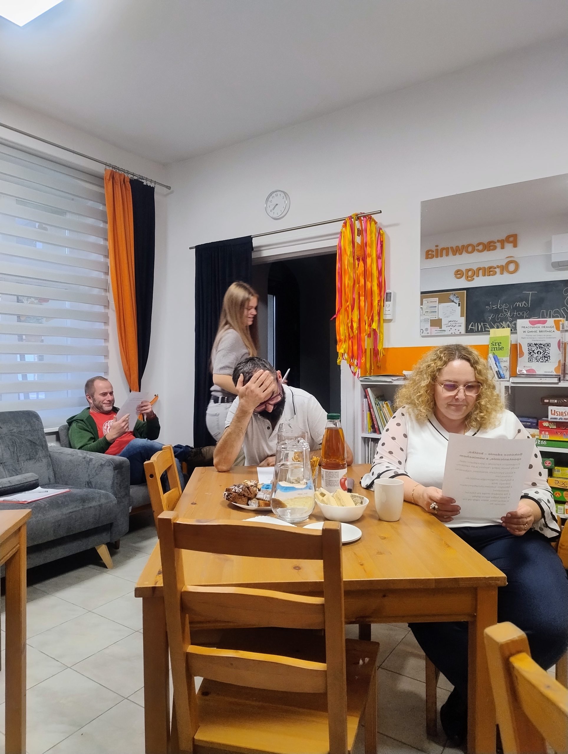 na zdjęciu widoczni są uczestnicy spotkania miedzypokoleniowego, którzy siedzą przy stole i na fotelu