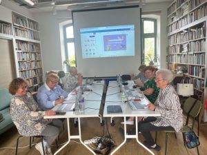 Uczestniczki kursu przy stole pracują na laptopach, w tle ekran
