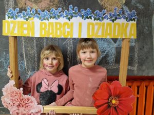 dwie dziewczynki w ramce drewnianej i ozdobionej własnoręcznie kwiatami z papieru i napisem dzień babci i dziadka