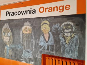 tablica ścienna, na której kredą narysowano podobizny babć i dziadka. u góry napis pracownia orange