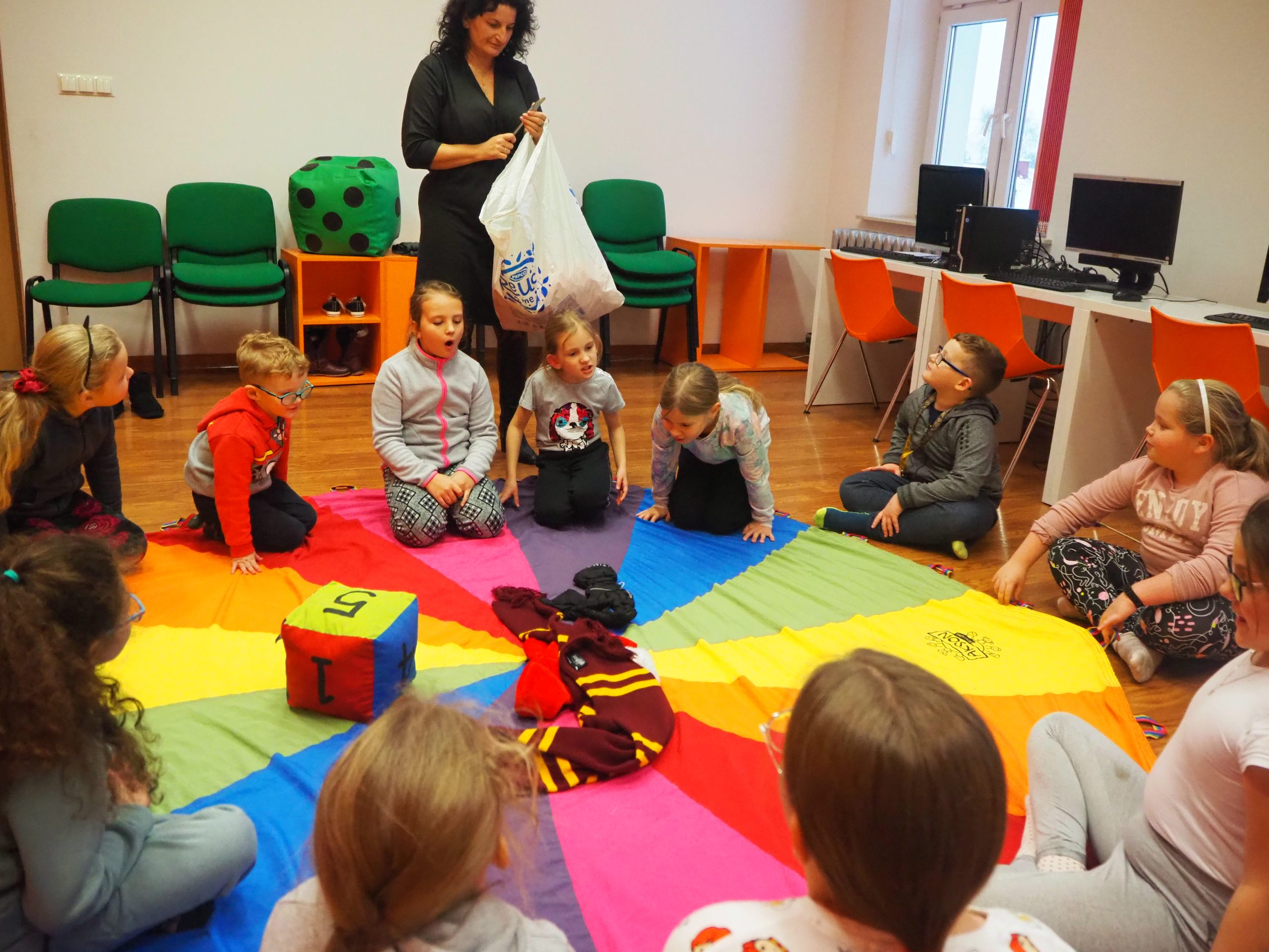 dzieci i prowadząca siedzą na podłodze na tęczowym materiale podczas zabaw warsztatowych