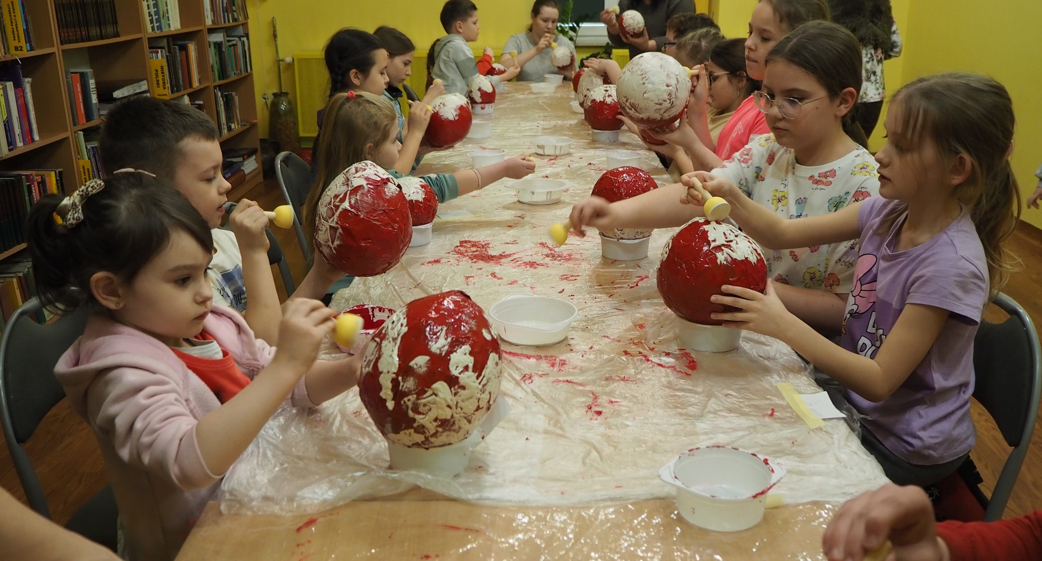 dzieci przy stole malują czerwone kule na biało