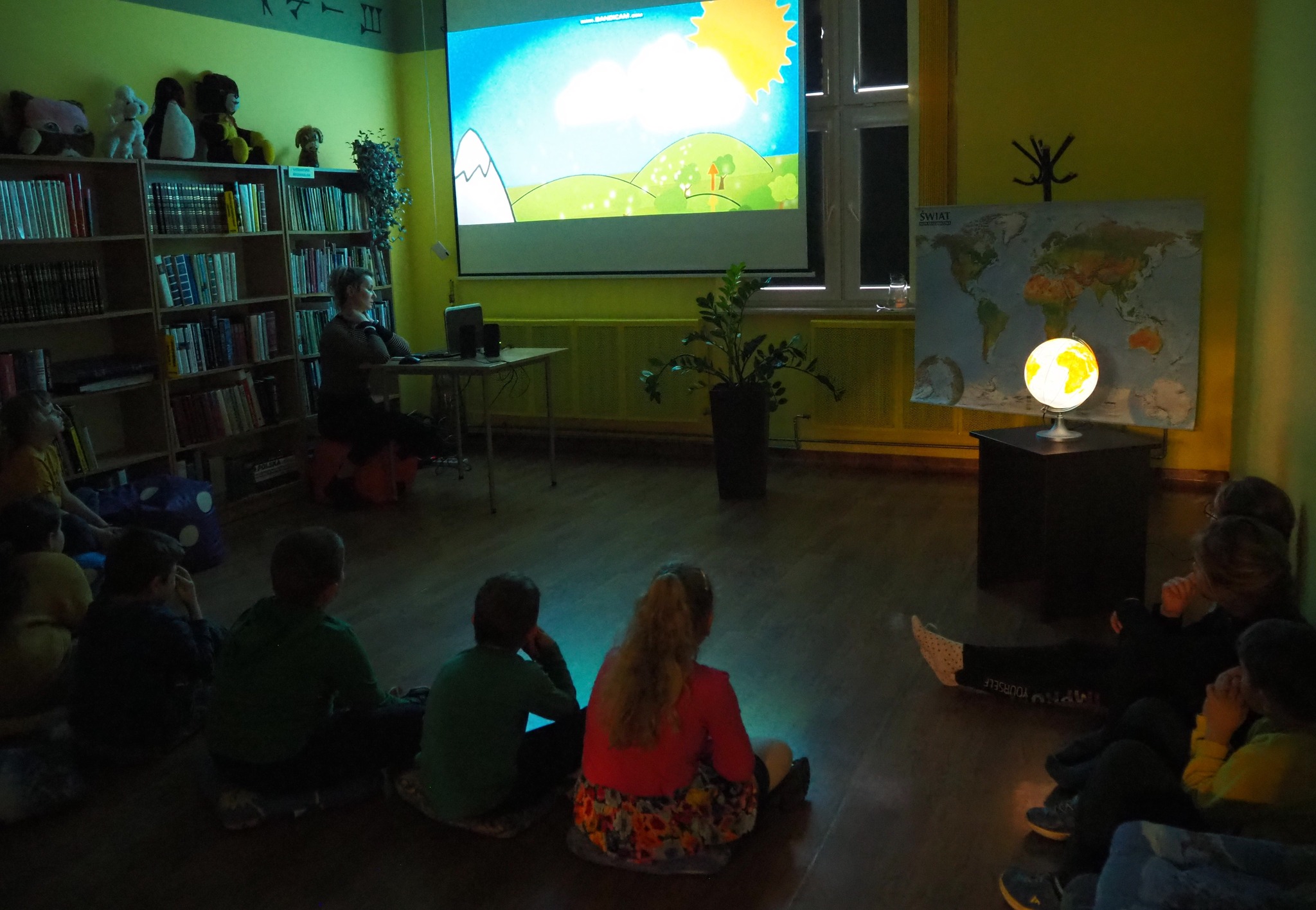 dzieci siedzą na podłodze w zacienionym pokoju i oglądają film z projektora