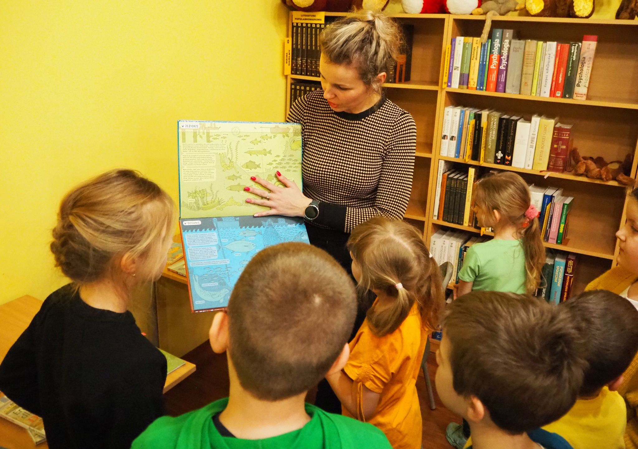 dzieci stoją obok kobiety która pokazuje im książkę