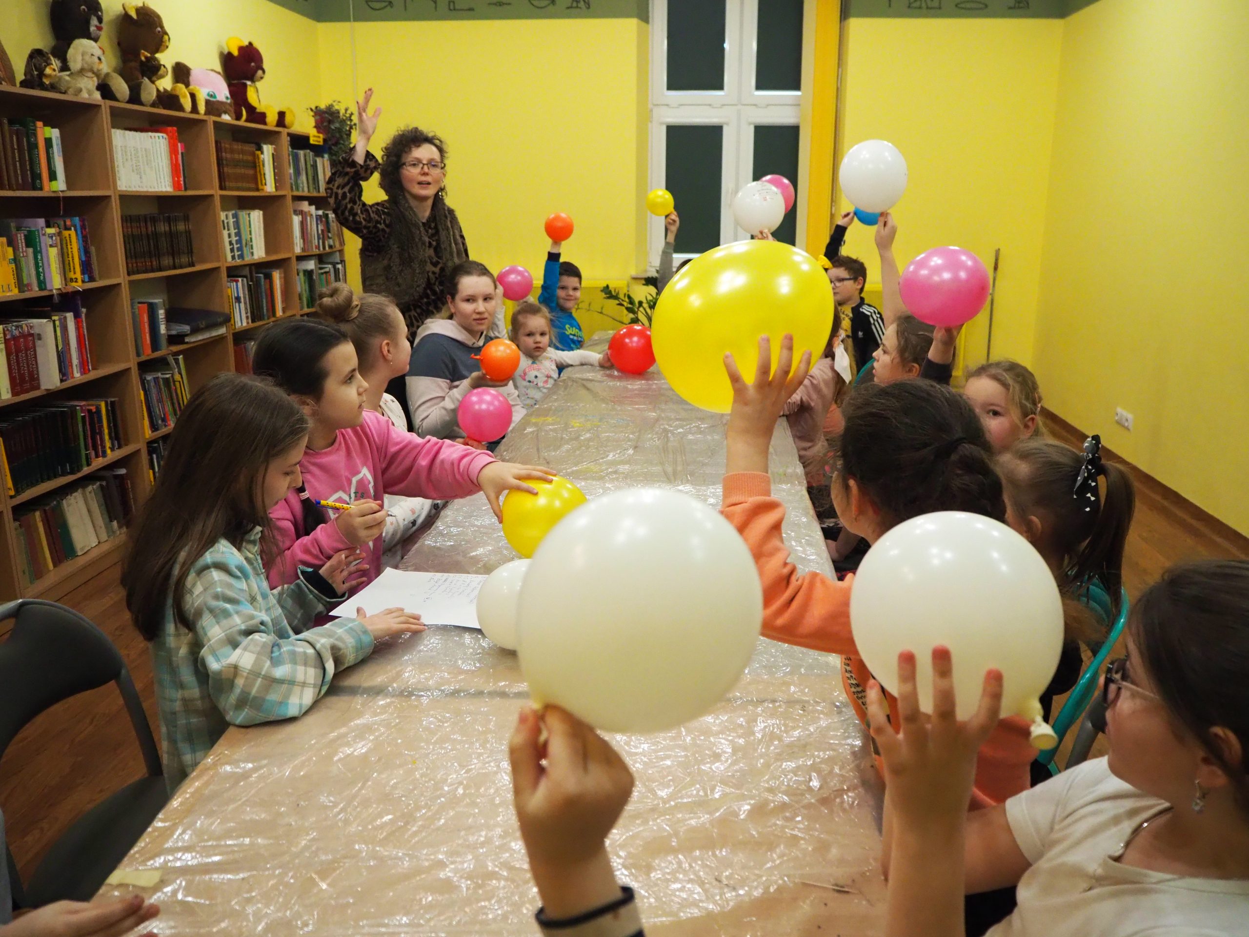 grupa dzieci przy stole unosi do góry kolorowe balony