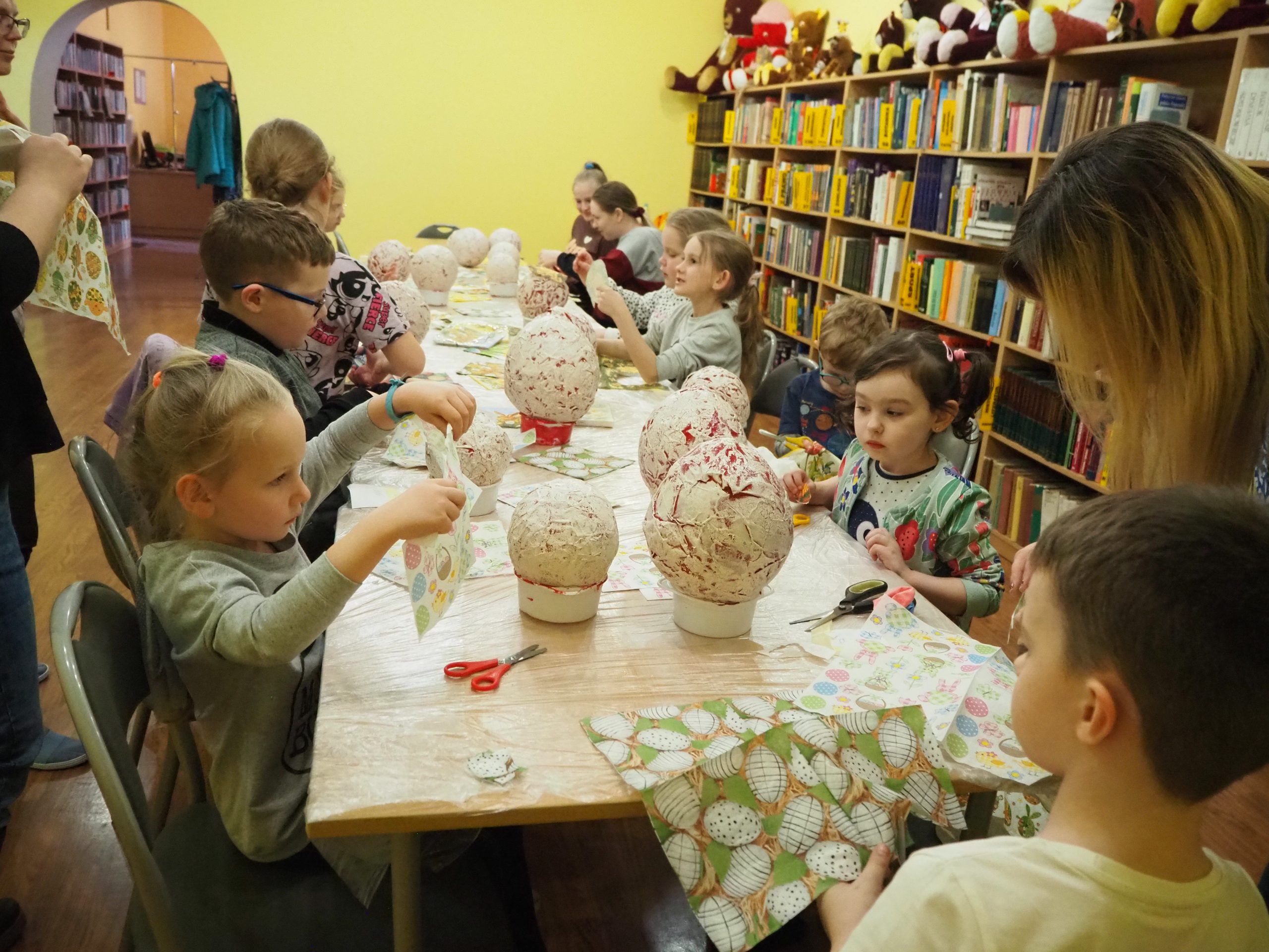 grupa dzieci przy stole wycina elementy z serwetek które później przykleją na papierowe jajka