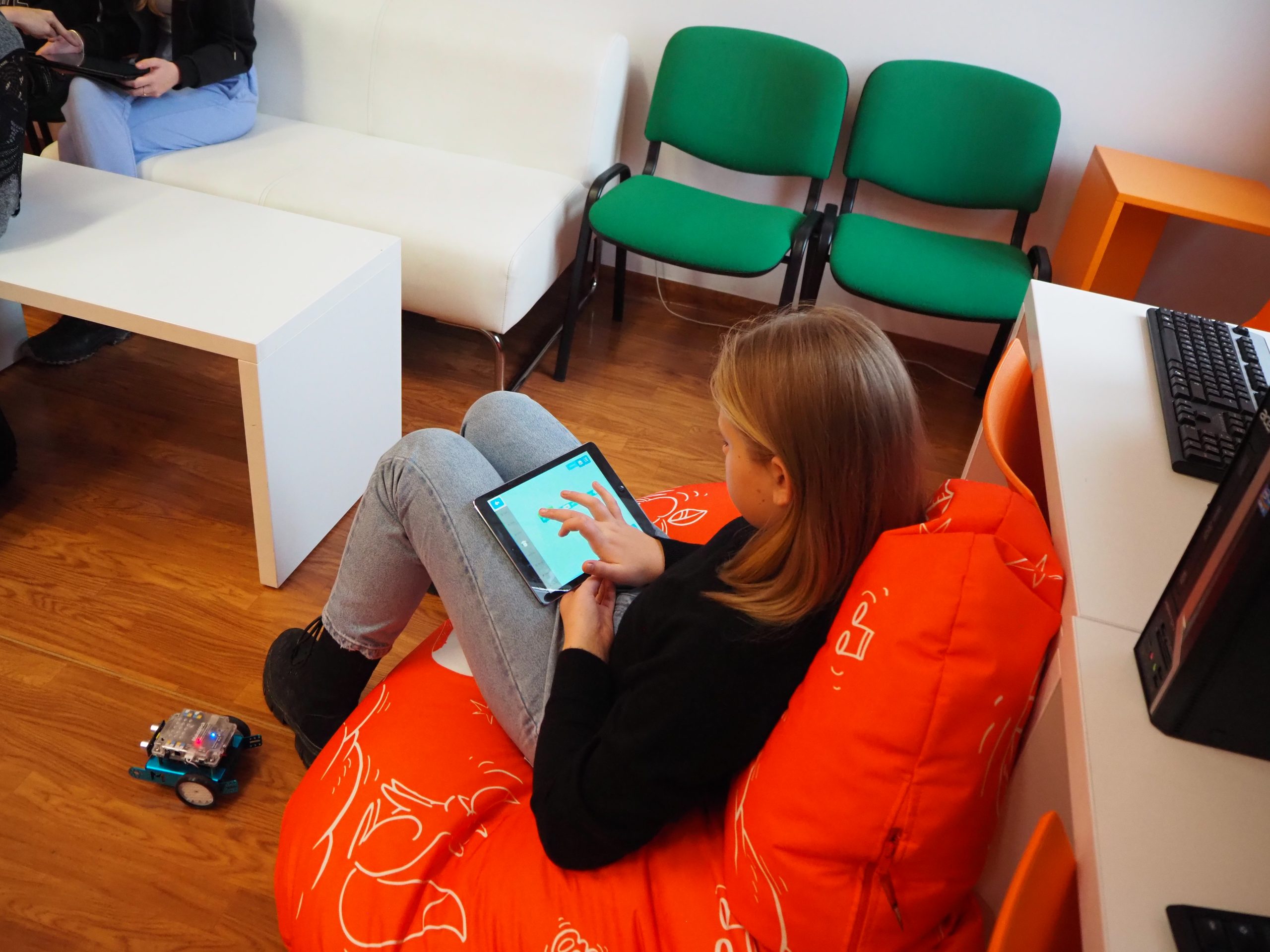 dziewczyna siedzi na pomarańczowej pufie i korzysta z tabletu
