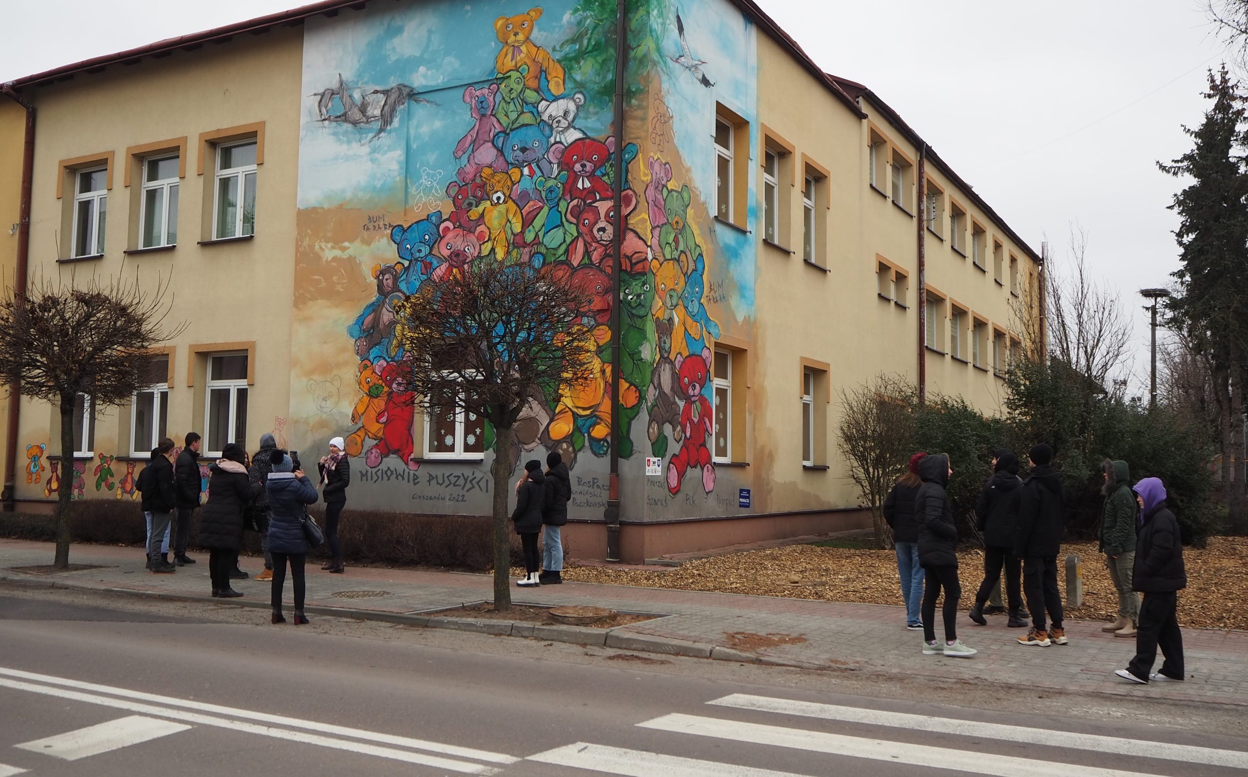 zdjęcie młodzieży przy budynku z muralem z wizerunkiem kolorowych misiów