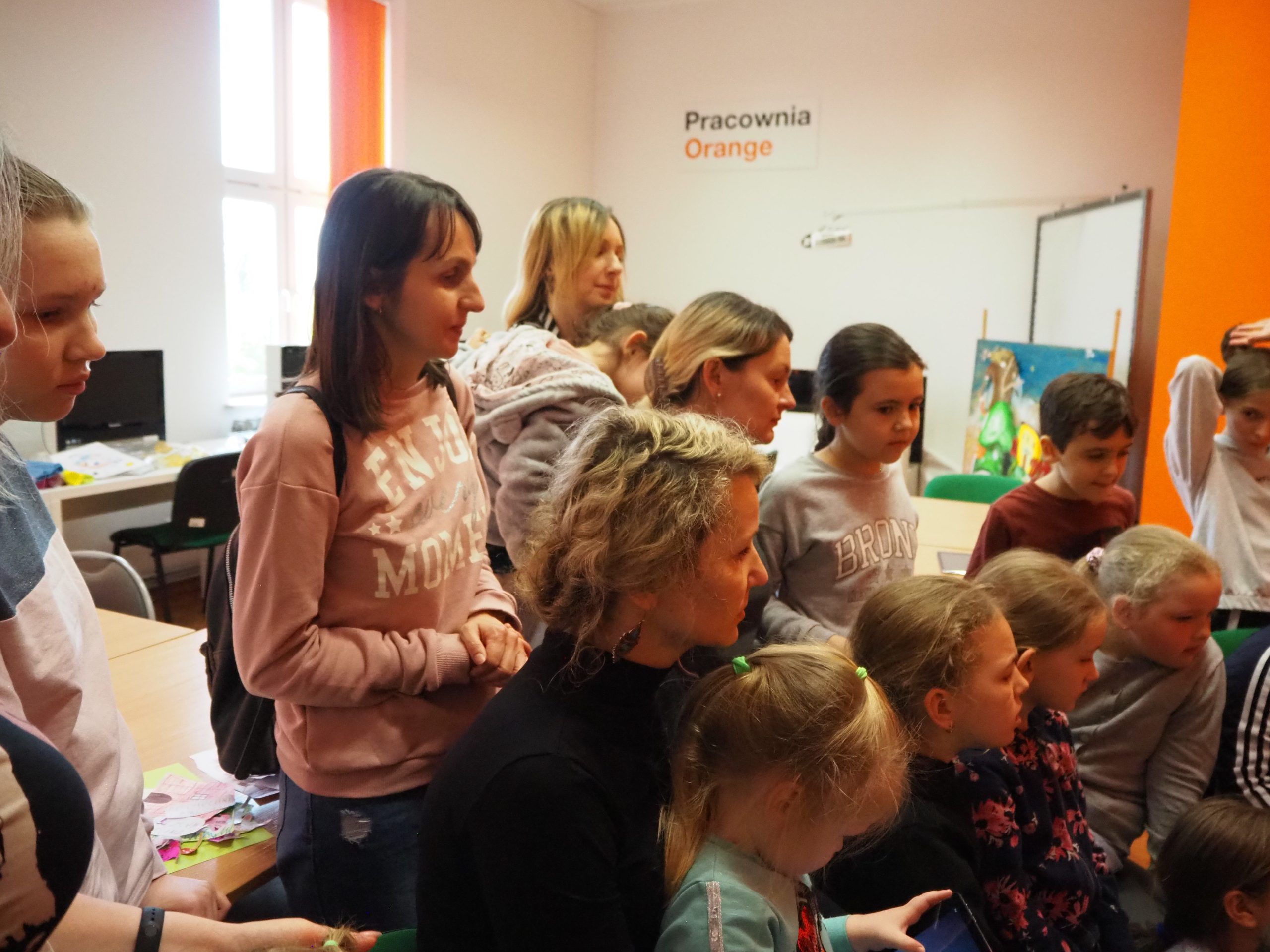 dzieci i cztery dorosłe kobiety w pracowni orange siedzą w grupie