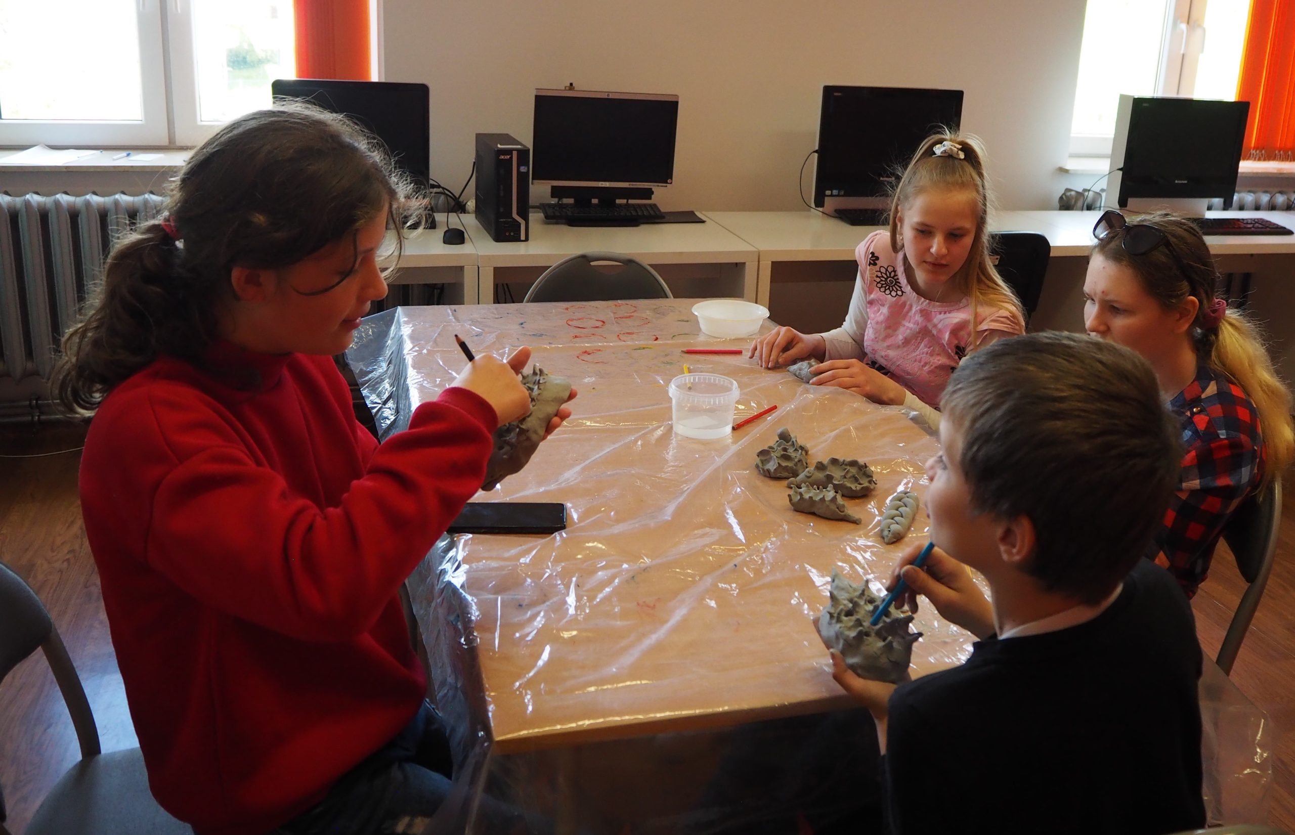 dzieci przy stole malują gliniane jeżyki
