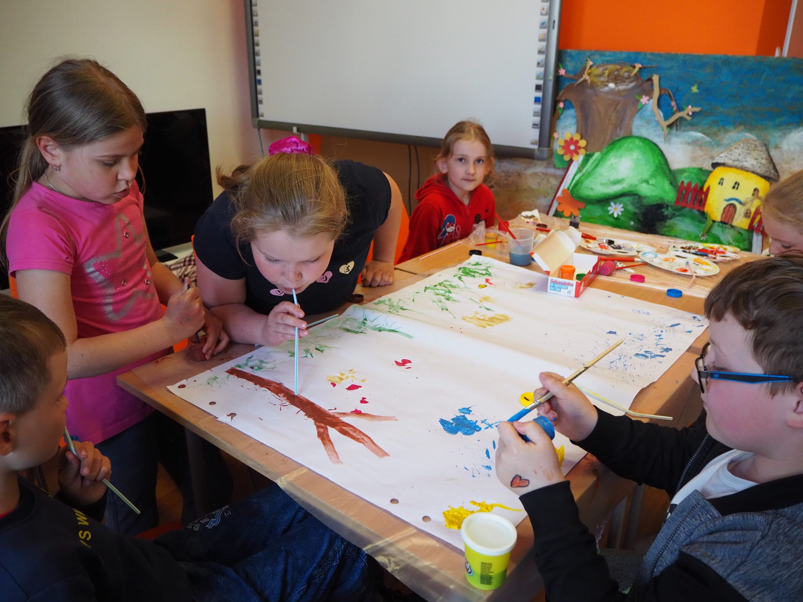 na zdjęciu grupa dzieci wspólnie maluje obrazek jedna z dziewczynek przy użyciu słomki rozdmuchuje farbę