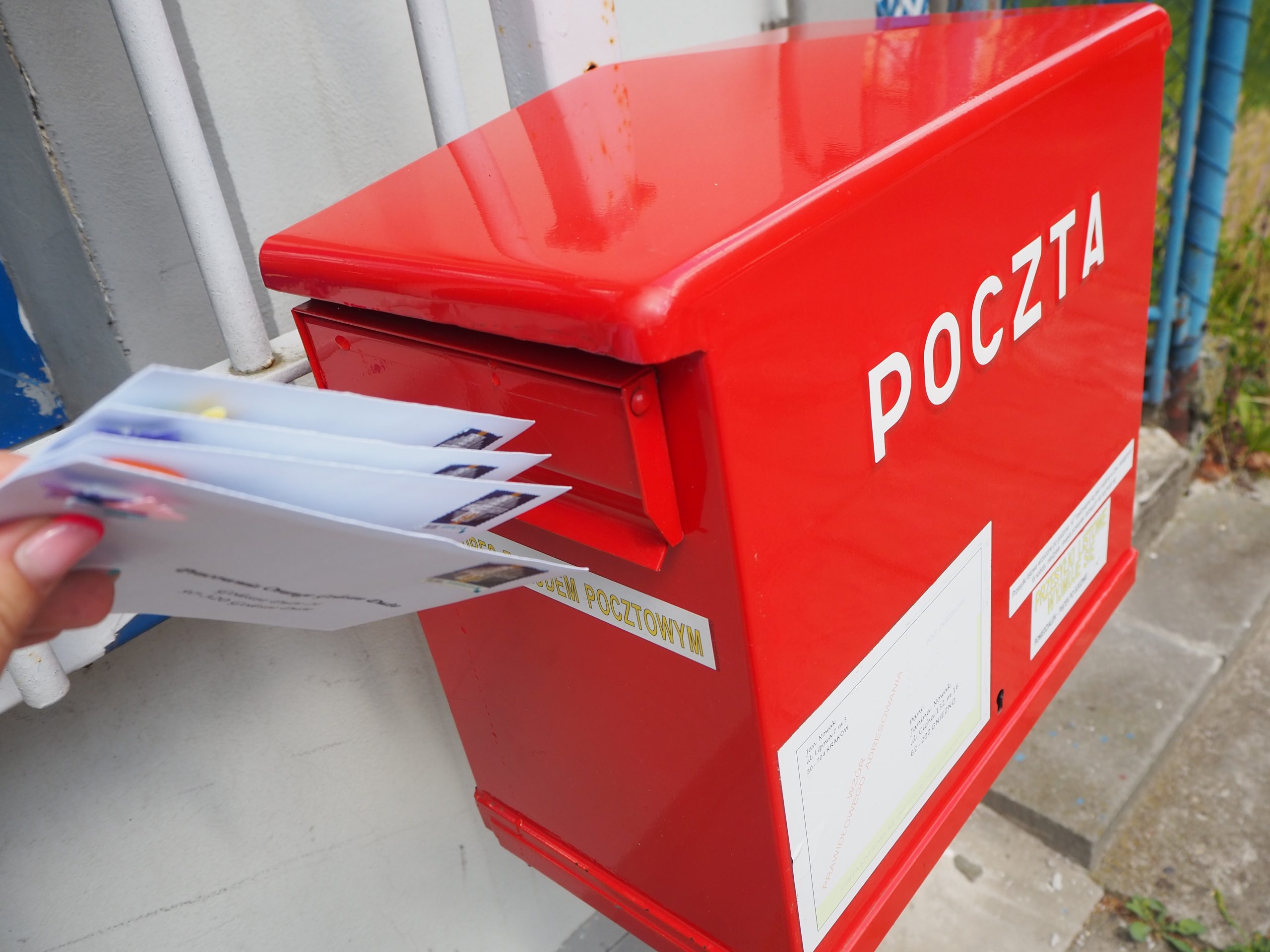 na zdjęciu czerwona skrzynka z napisem poczta do której ktoś wrzuca cztery listy