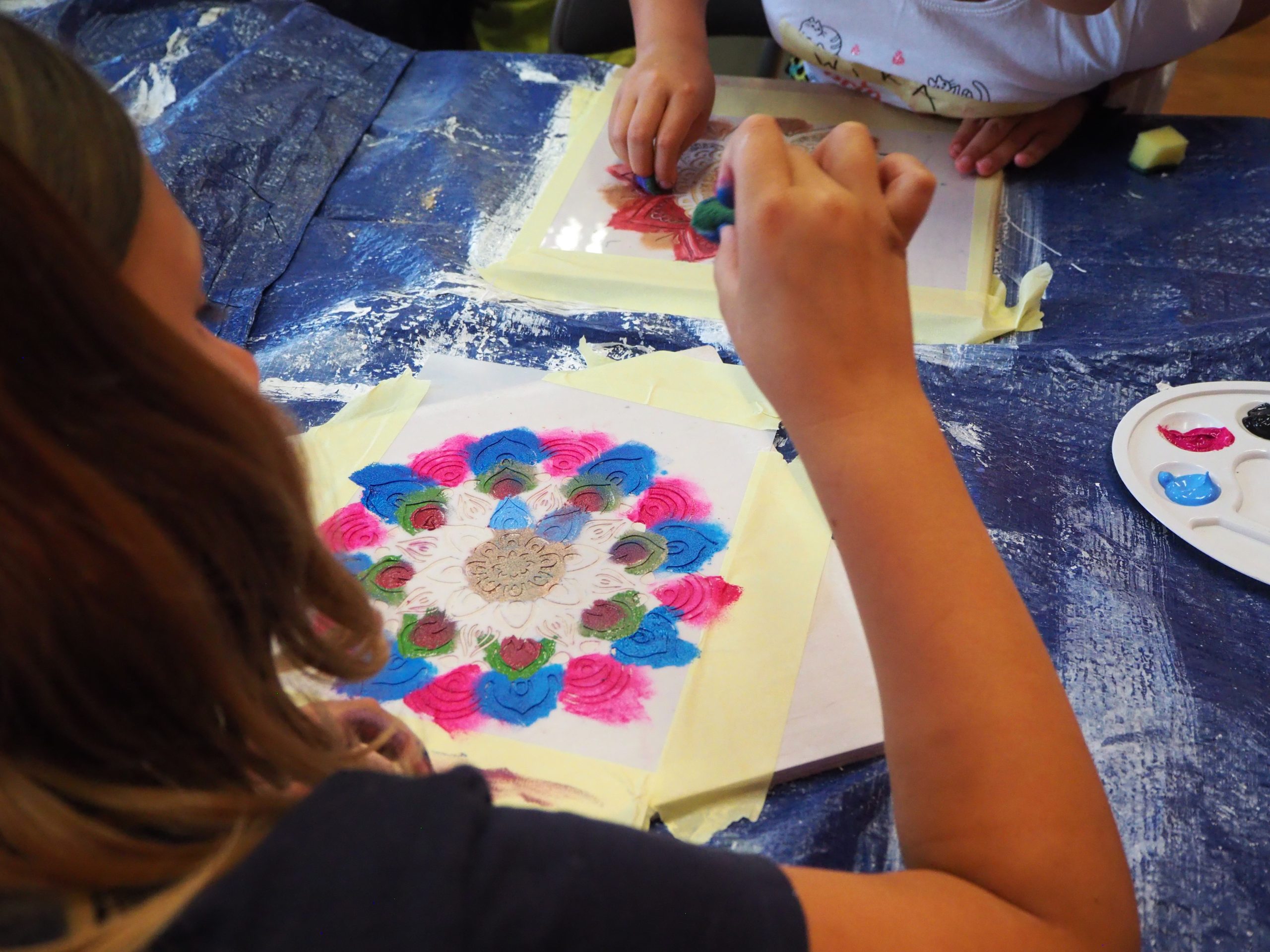 dziewczynka odbija mandale z szablonu przy pomocy gąbeczki i kolorowych farb