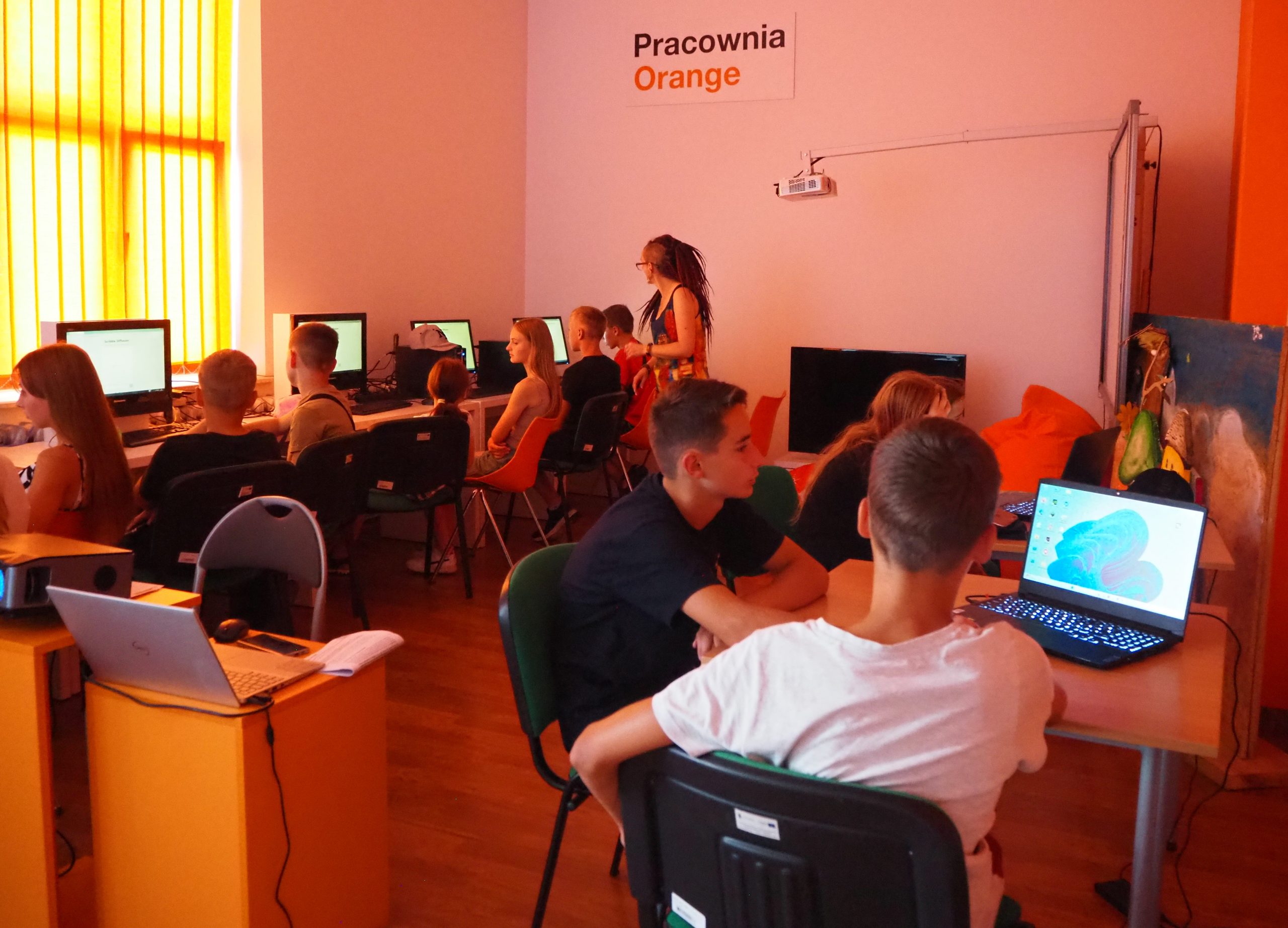 grupa osób w pracowni orange siedzi przy komputerach
