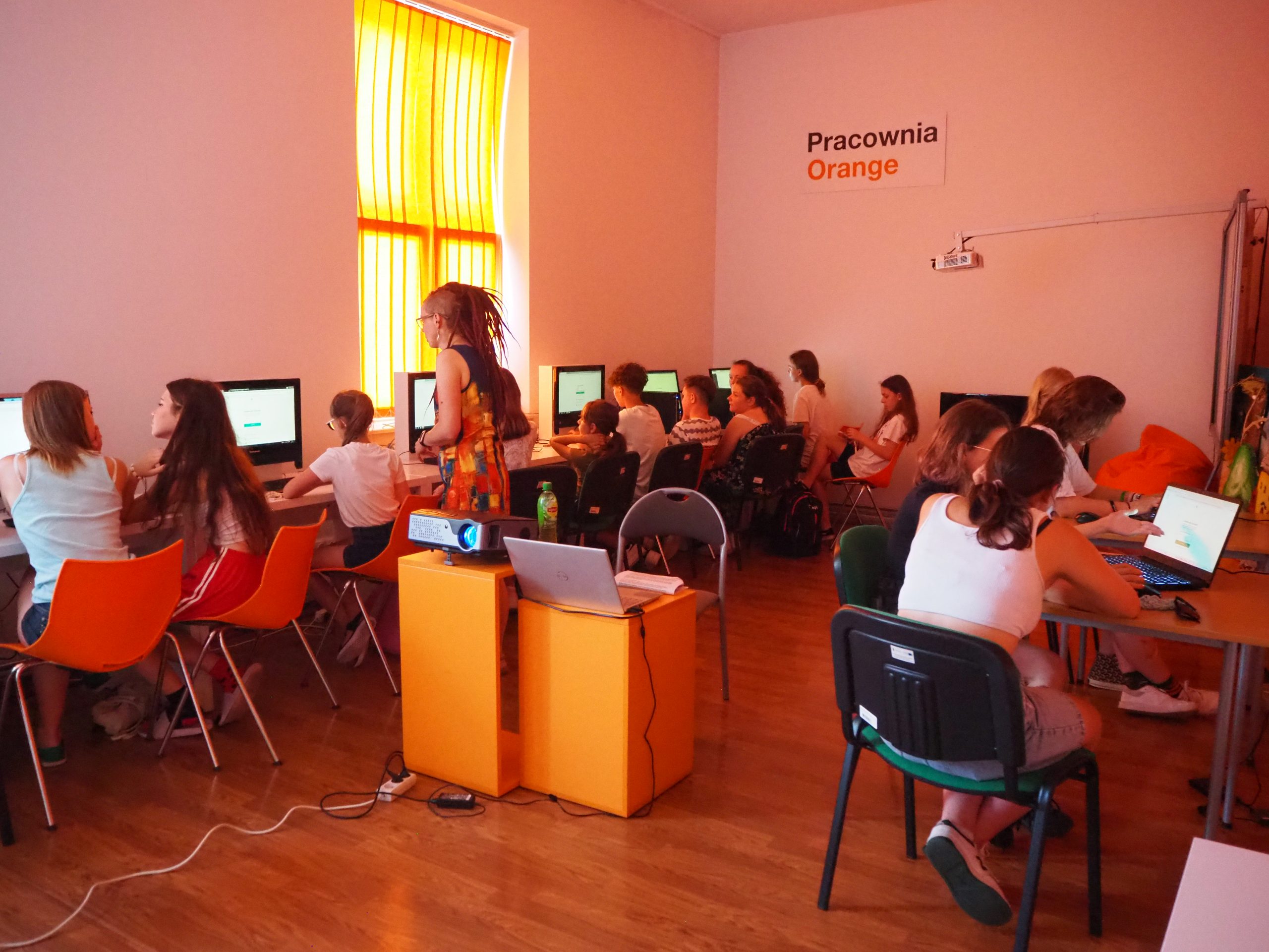 grupa osób siedzi przy komputerach w pracowni orange