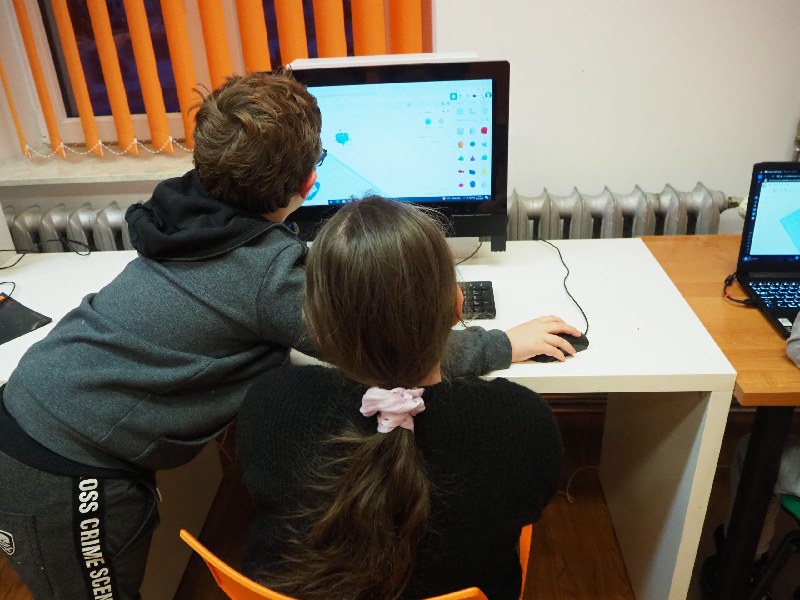 Chłopiec i dziewczynka siedzą przy komputerach.