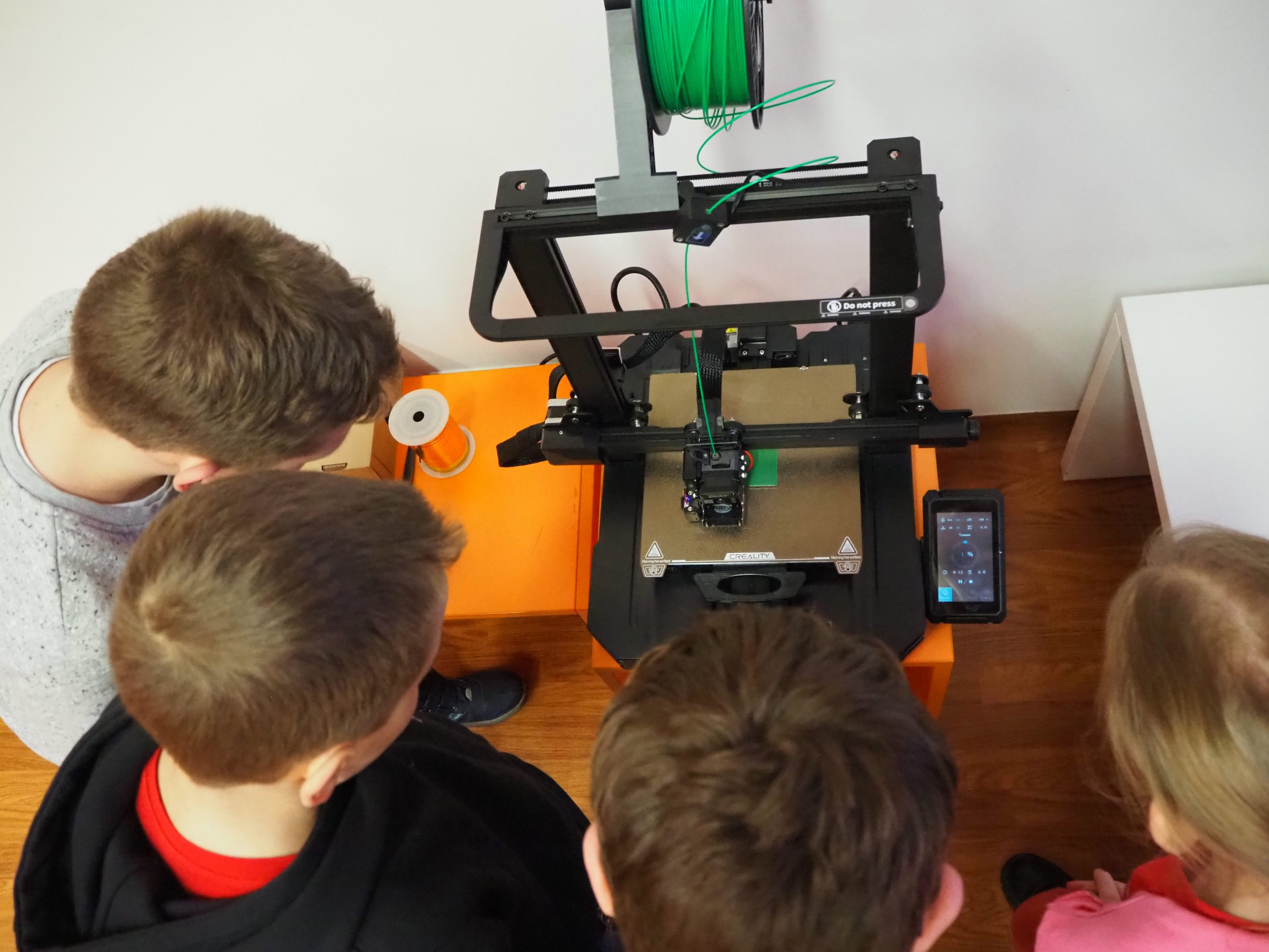 Dzieci obserwują pracę drukarki 3D.