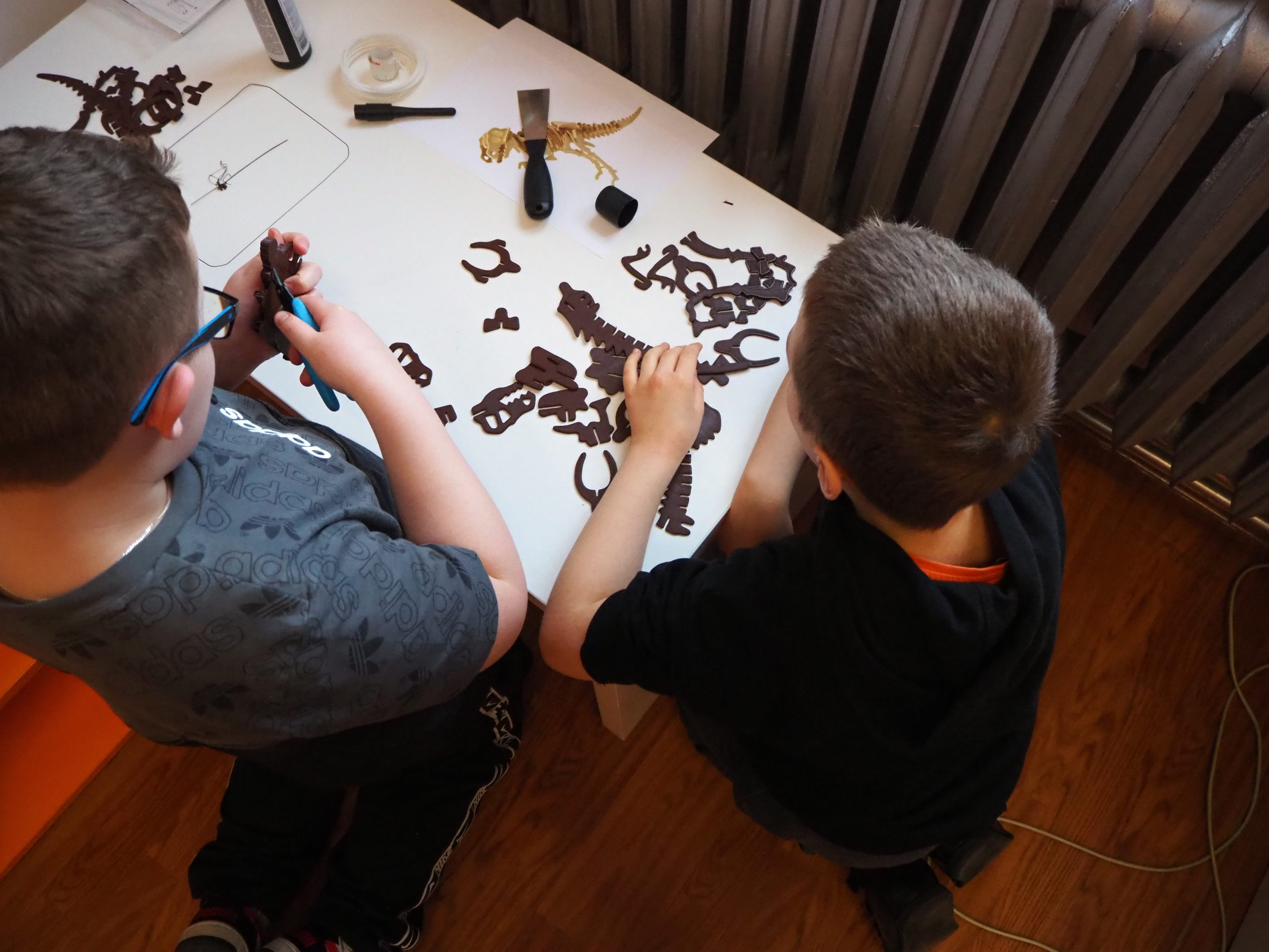 Dwa chłopcy przy stole z wyciętymi fragmentami szkieletu dinozaura.