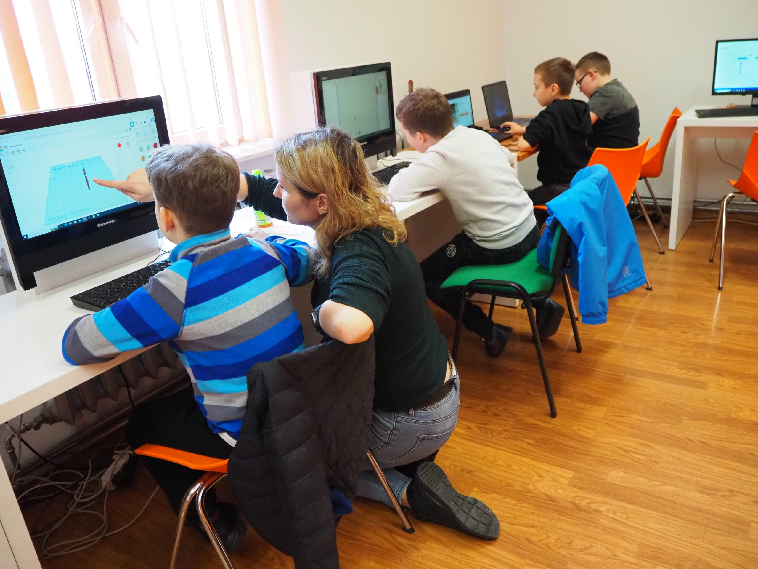 Grupa dzieci wraz z prowadzącą projektują szkielet dinozaura na komputerze.