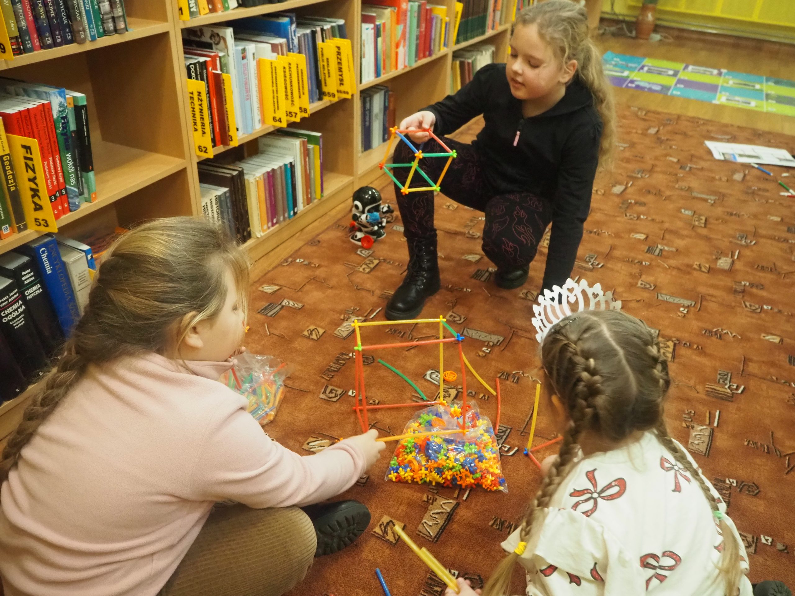 dzieci siedzą na dywanie i budują konstrukcje ze słomek