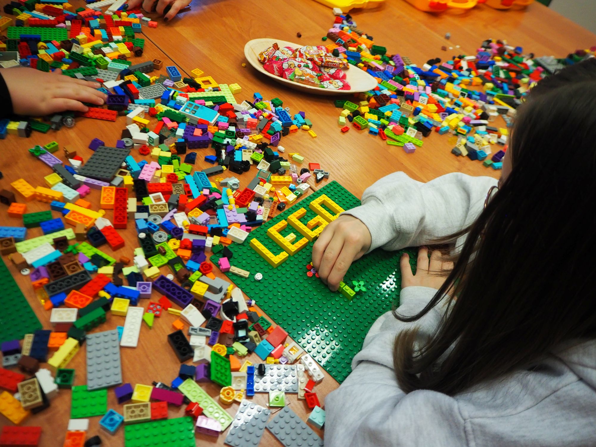 na stole leży dużo klocków lego i dziewczynka która coś układa
