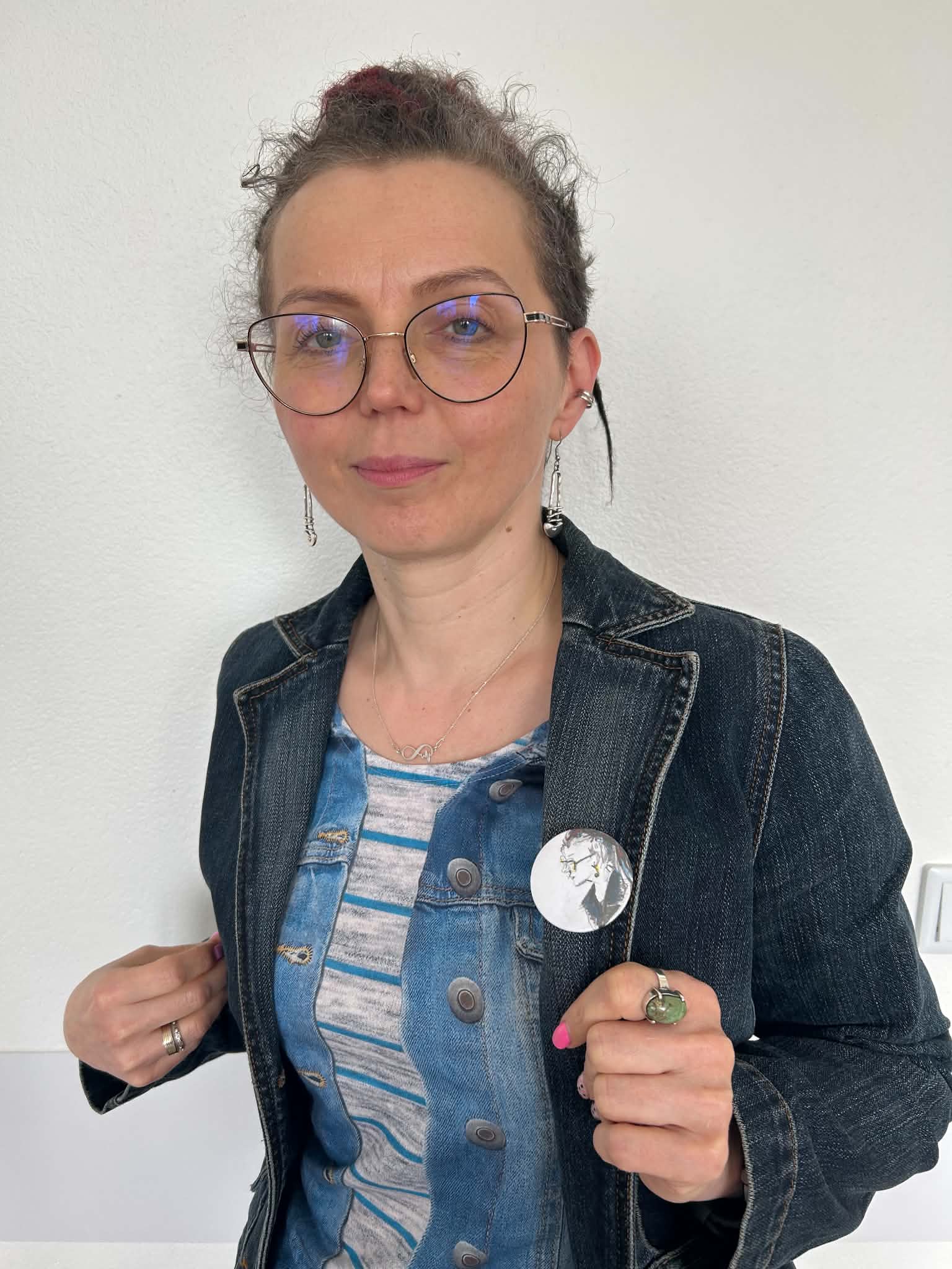 Pani dyrektor biblioteki pokazuje przypinkę przyczepioną na kurtce, wykonana przez uczestnika zajęć