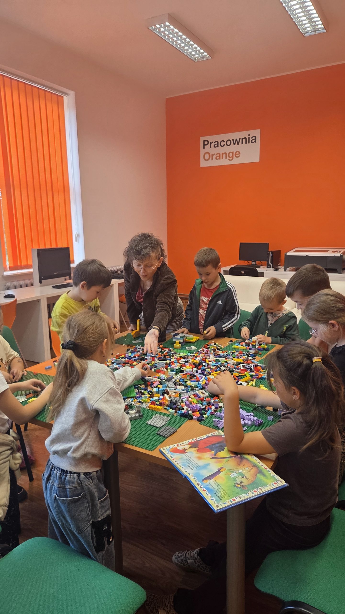 dzieci stojące przy stole na którym znajduje się dużo klocków lego