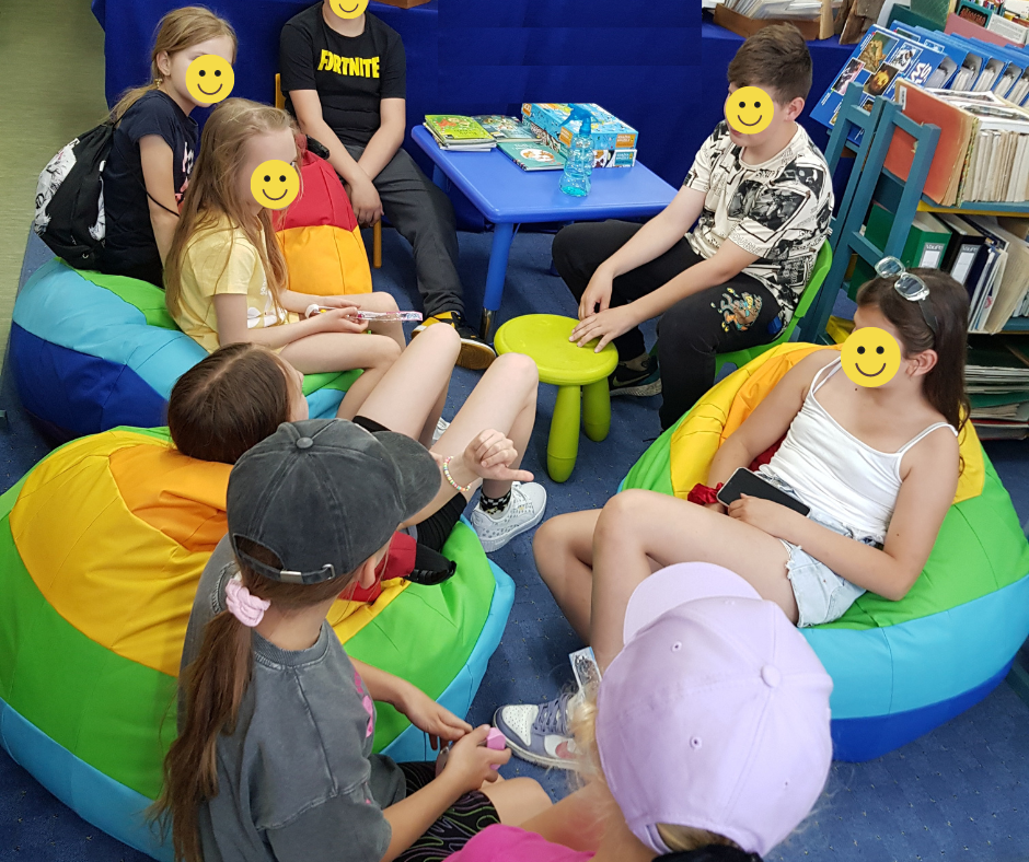 Grupa dzieci siedzi na kolorowych poduchach.