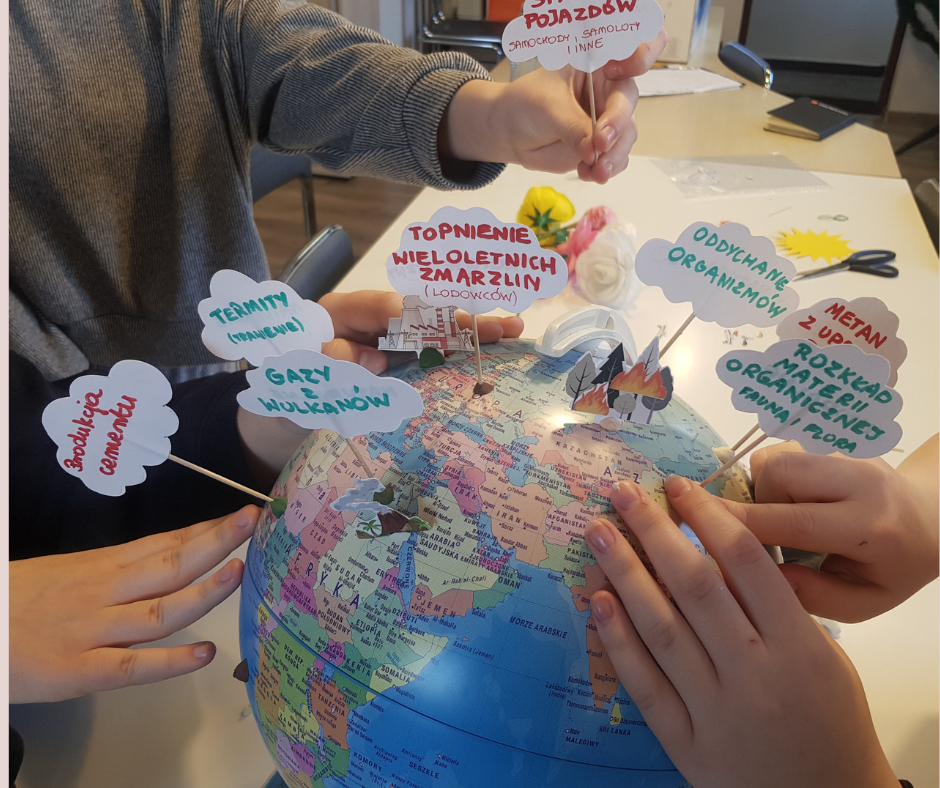 Globus, wokół którego widać ręce młodzieży umieszczające na nim chmurki z zapisanymi informacjami o źródłach gazów cieplarnianych.