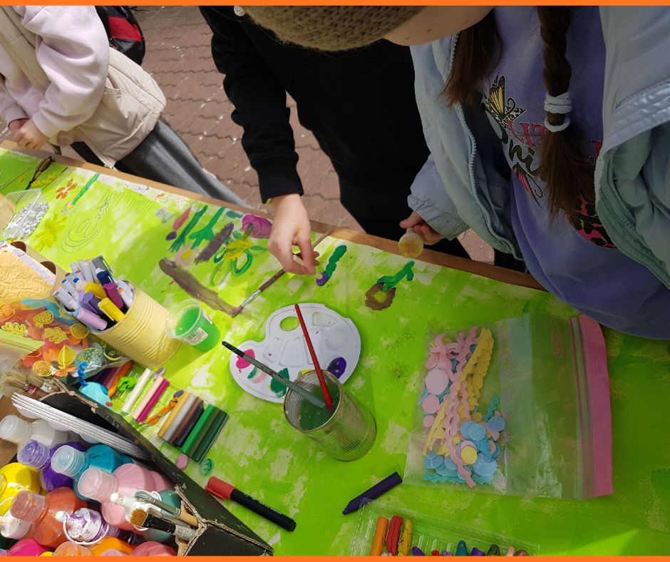 dzieci stojące przy stole i malujące łąkę