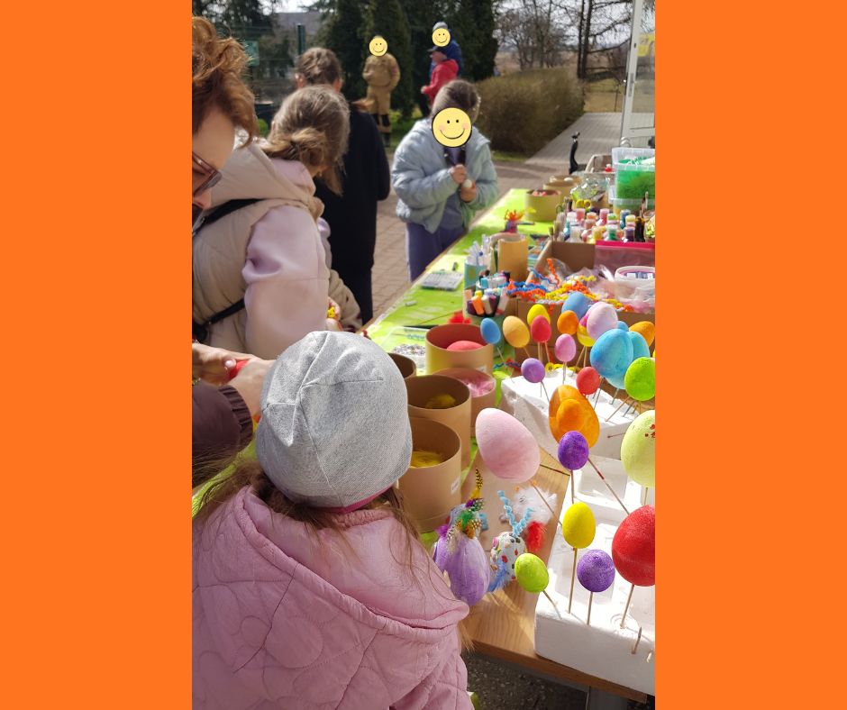 Dzieci stojące na świeżym powietrzu przy stole na którym znajdują się media plastyczne